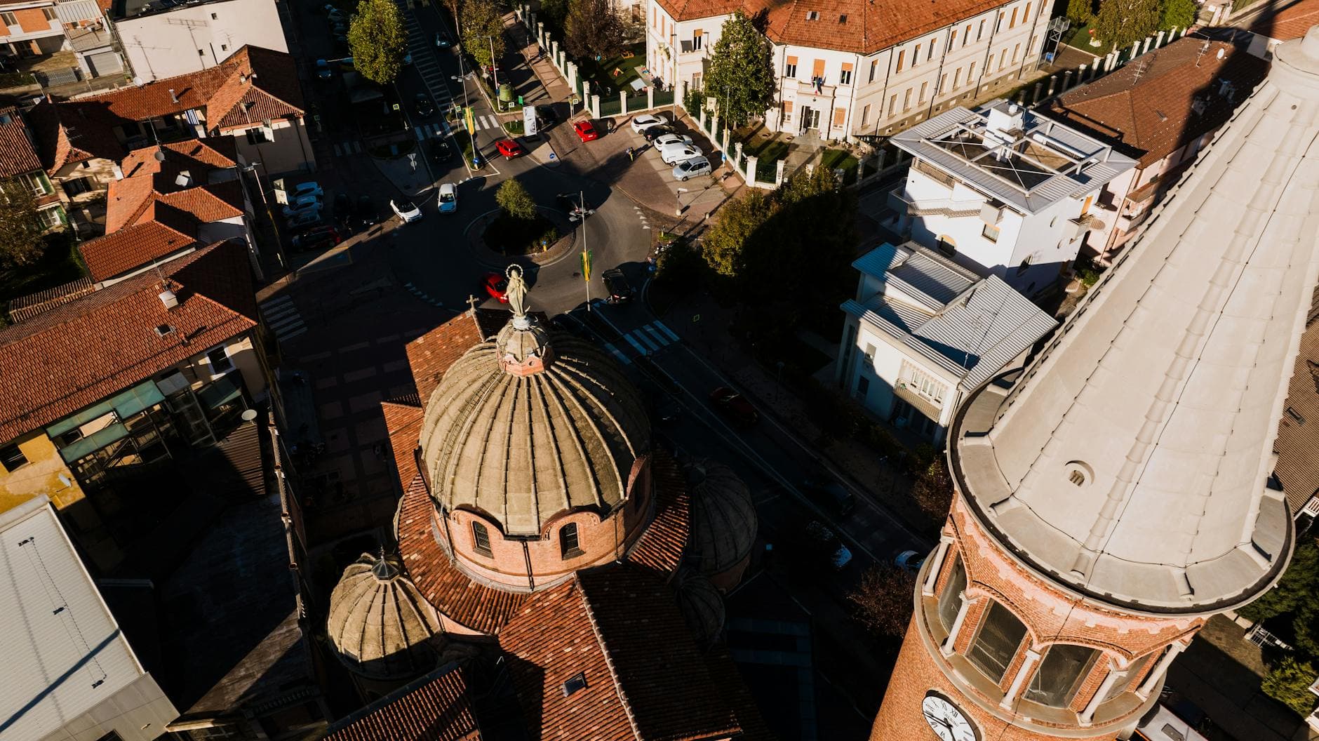 Drone view of Alba, Italy showcasing church domes and urban streets in vibrant sunlight.