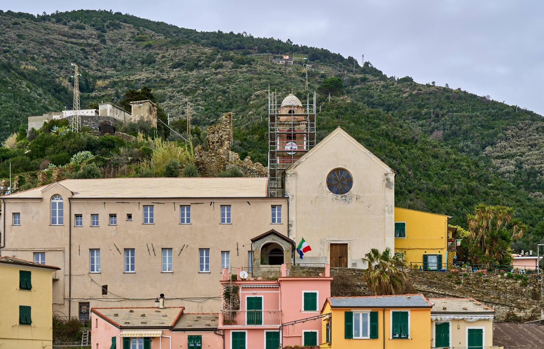 Picturesque view of colorful houses and historic church in Vernazza with lush hills in the background.