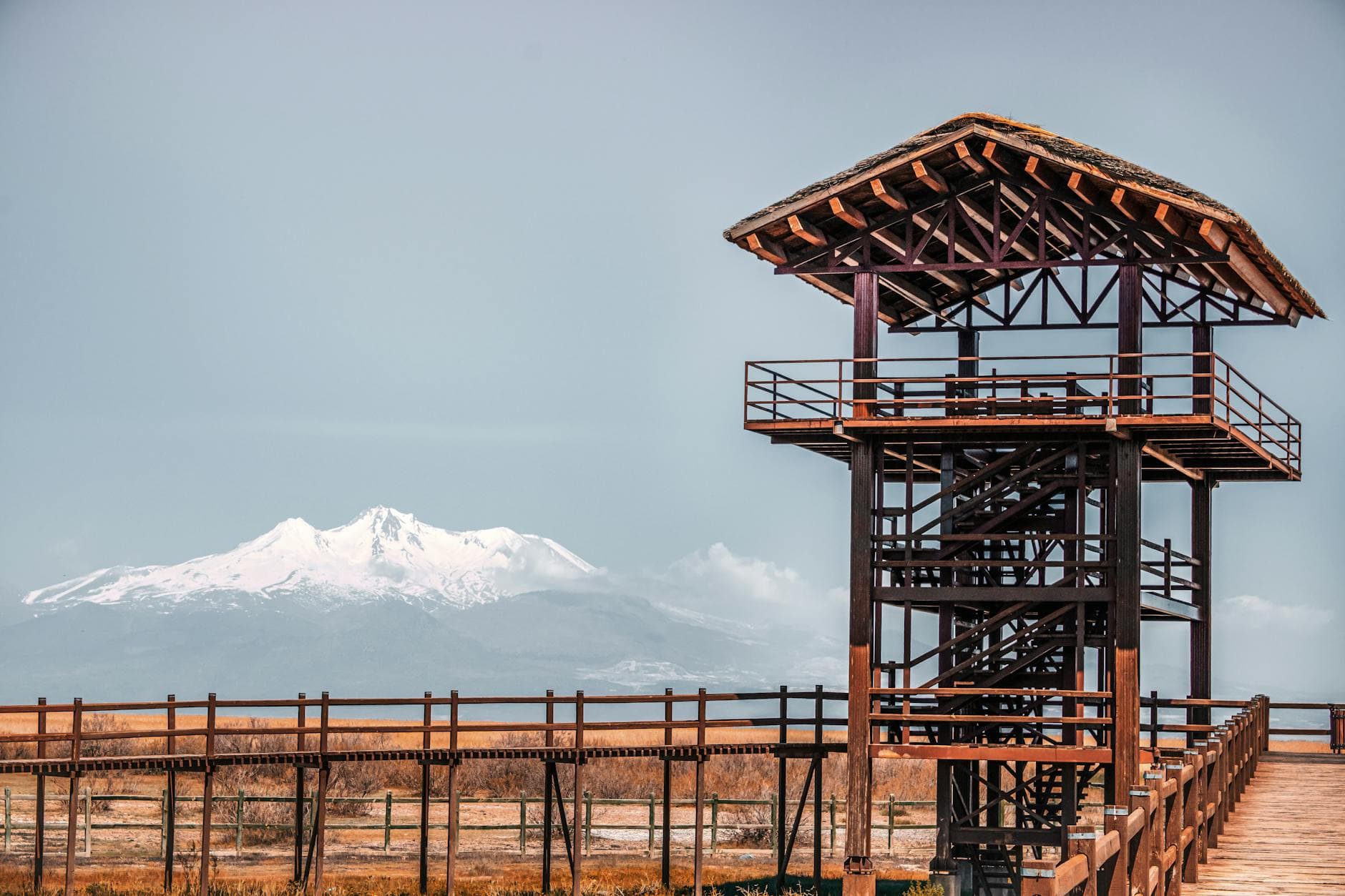 Scenic view of a wooden observation tower and boardwalk with snowy Mount Erciyes in the background, Kayseri, Türkiye.