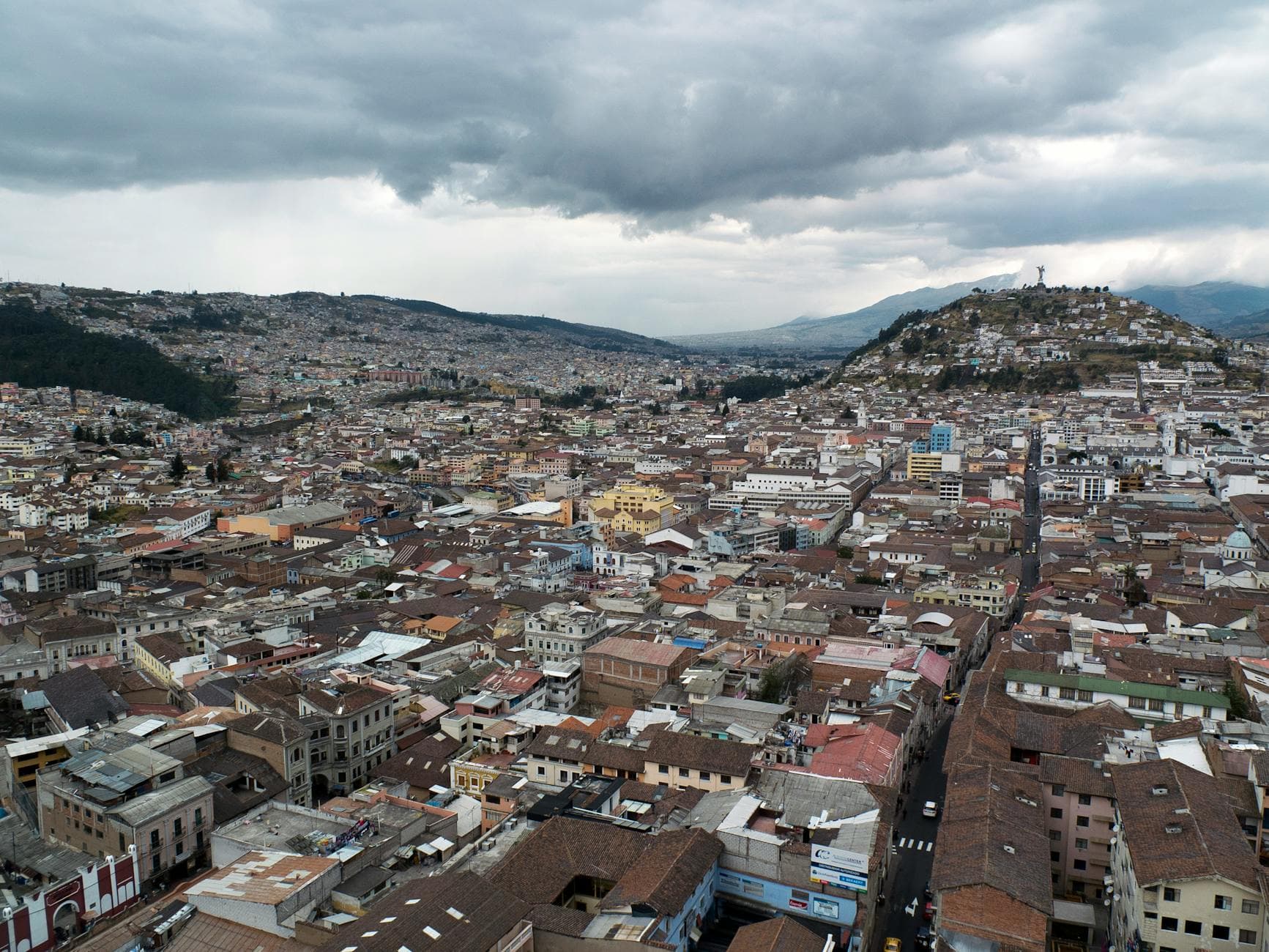Expansive aerial view of Quito's historic cityscape with cloudy skies, featuring scenic hills and urban density.
