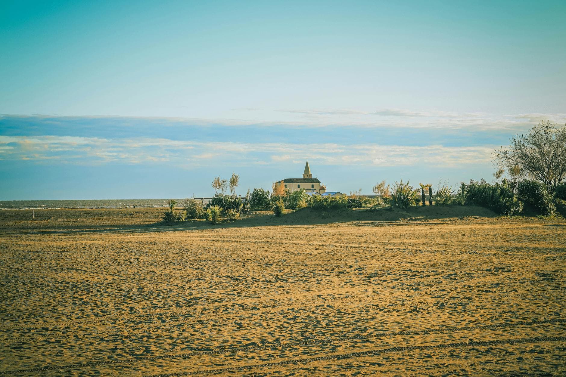 Serene sandy beach with a distant view of a church under a clear blue sky, evoking tranquility.