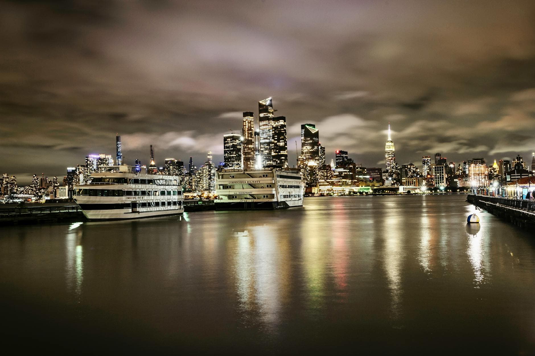 Stunning nighttime view of Midtown Manhattan skyline from Hoboken waterfront with boats and reflections.