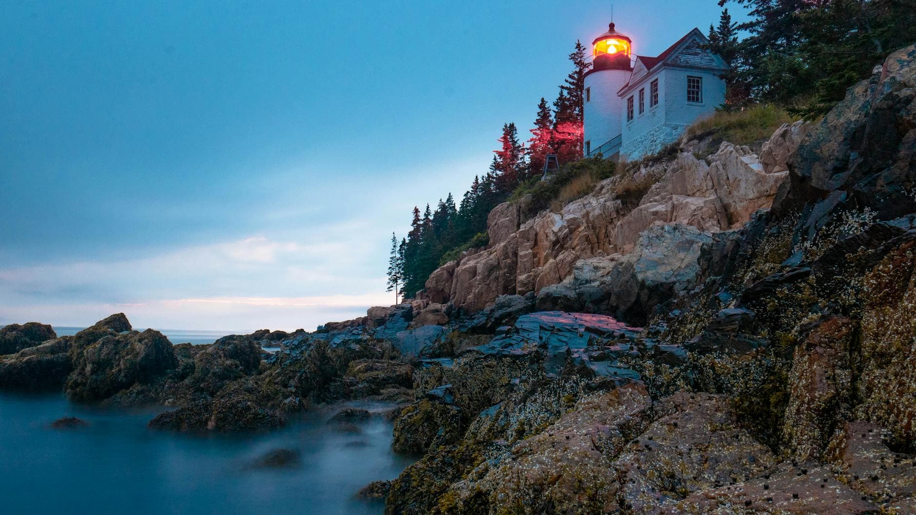 Scenic view of Bass Harbor Head Lighthouse on rocky coast at sunset in Acadia National Park, Maine.
