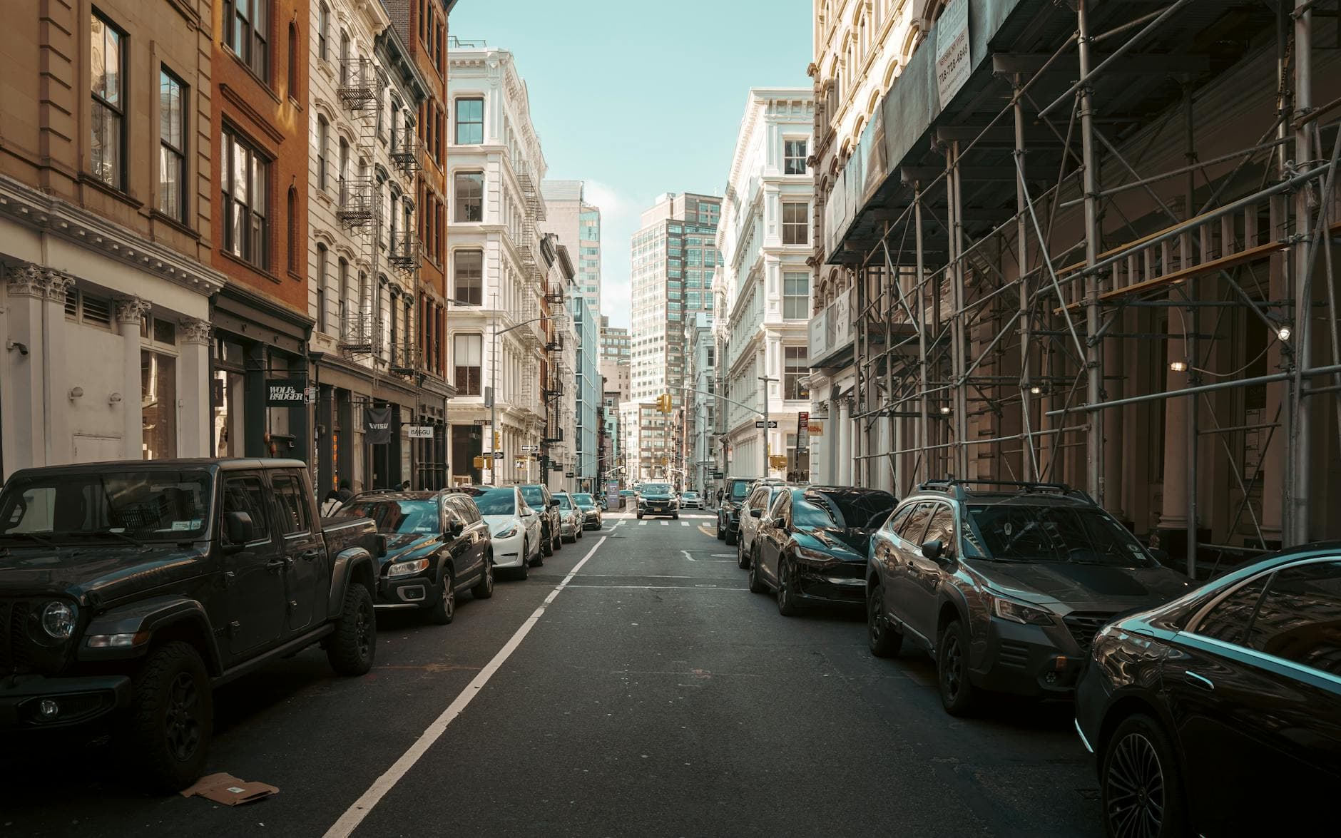 A bustling street in New York City with classic architecture and a variety of parked cars.