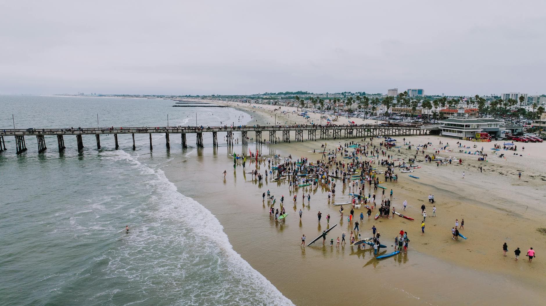 Aerial shot of a bustling beach day at Newport Beach Pier, capturing the lively summer scene.