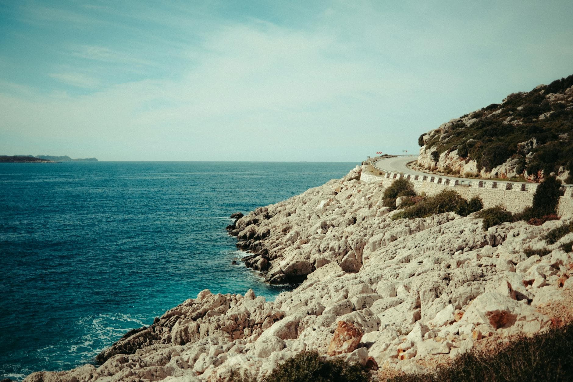 Breathtaking view of a winding coastal road along a rocky Mediterranean shoreline under a clear sky.
