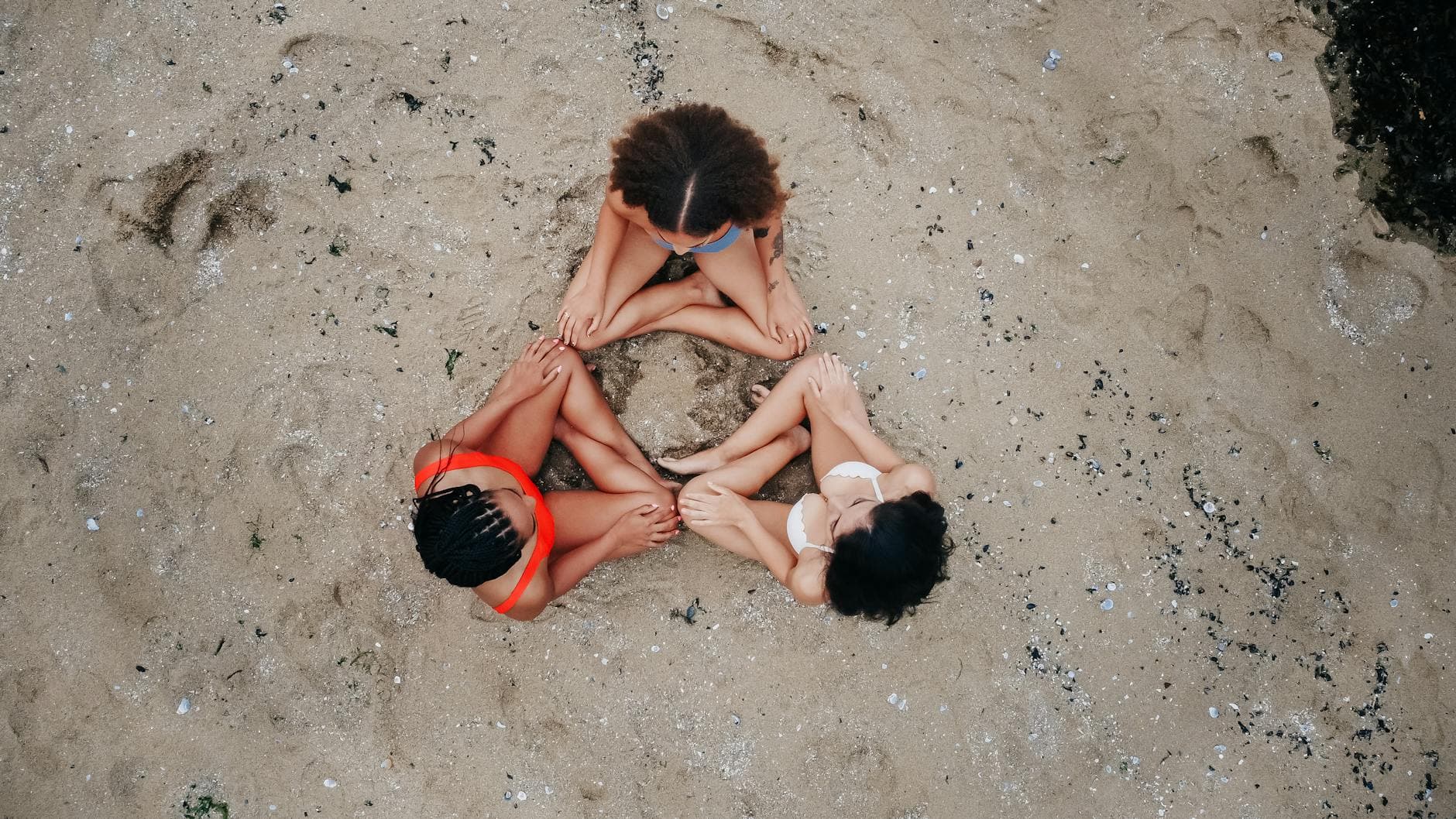 Aerial image of three friends sitting in a circle on a sandy beach in Vancouver, Canada.