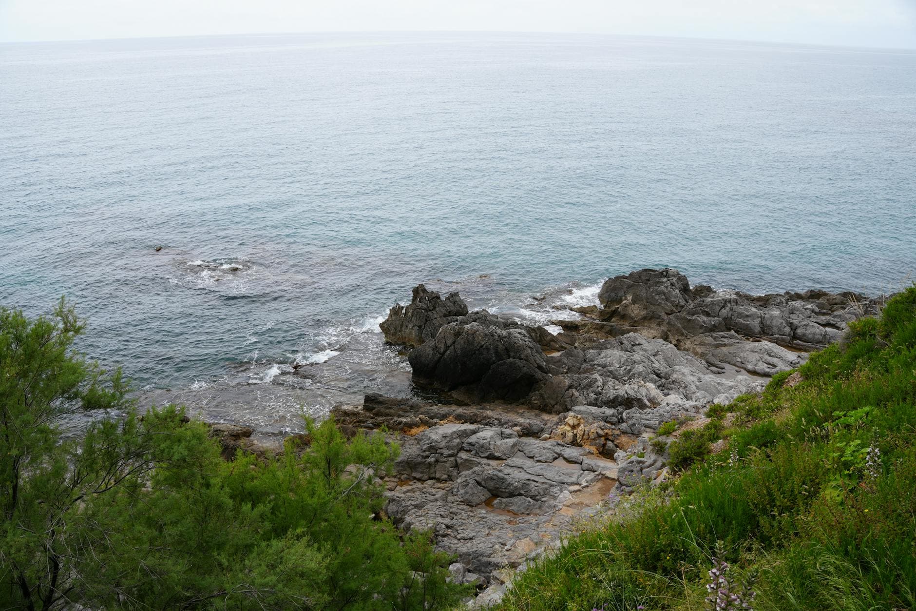 View of the rocky shoreline and blue sea at Cefalù, Sicily, Italy.