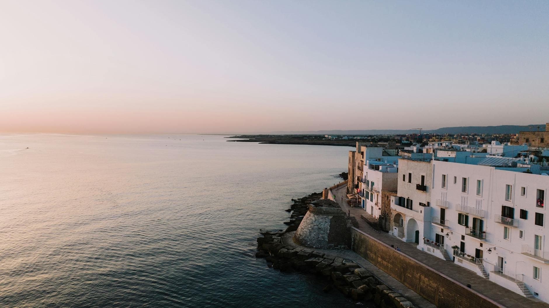 Aerial view of Monopoli's picturesque coastline in Puglia, Italy at sunset, showcasing vibrant architecture.