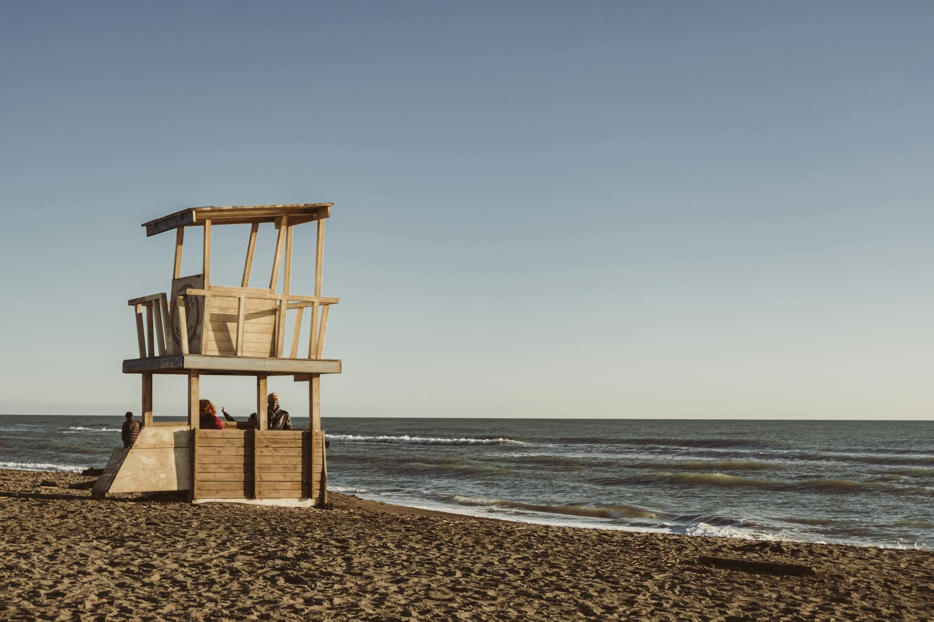 A serene beach with a wooden lifeguard tower overlooking the ocean at sunset.