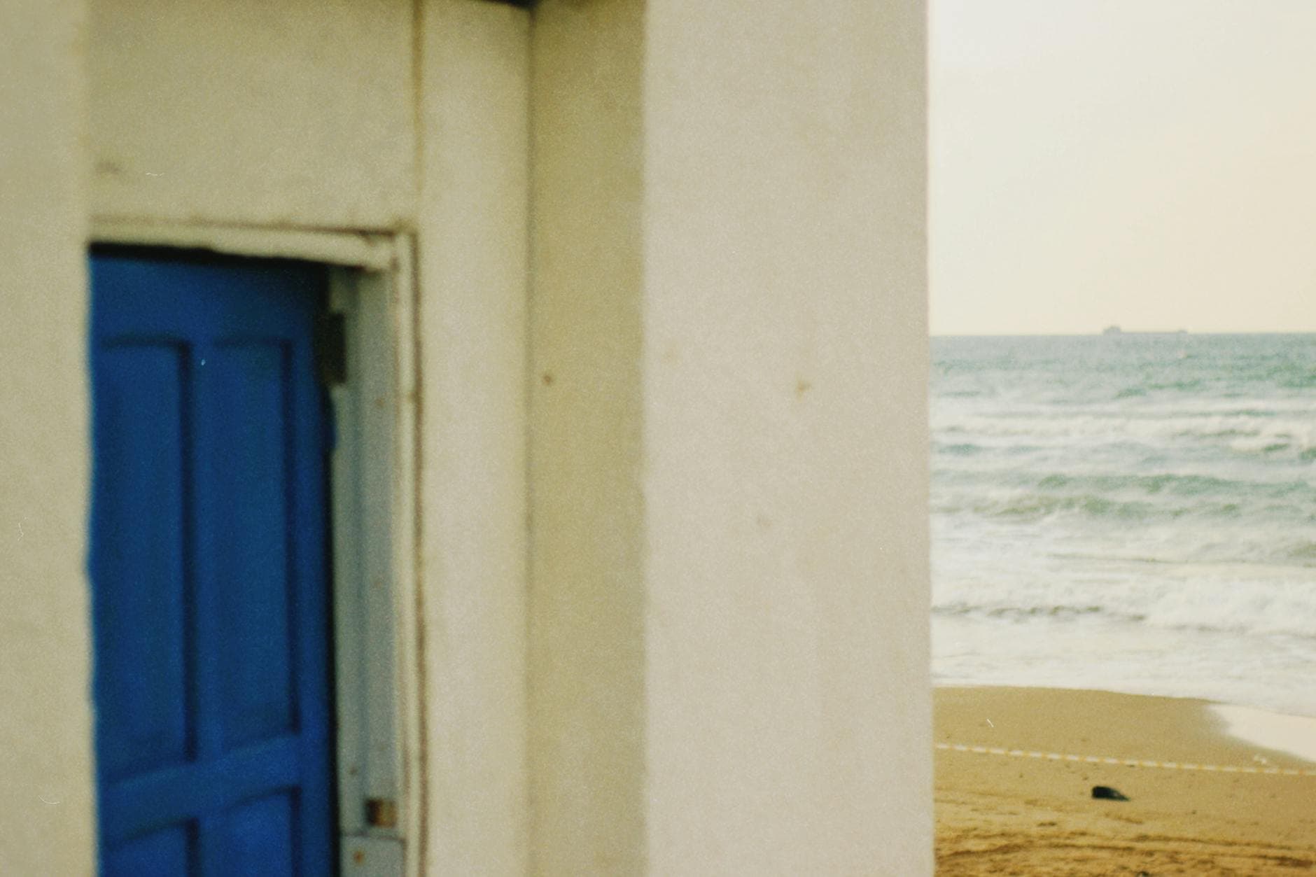 A serene view of the beach with a blue door building by the ocean waves.