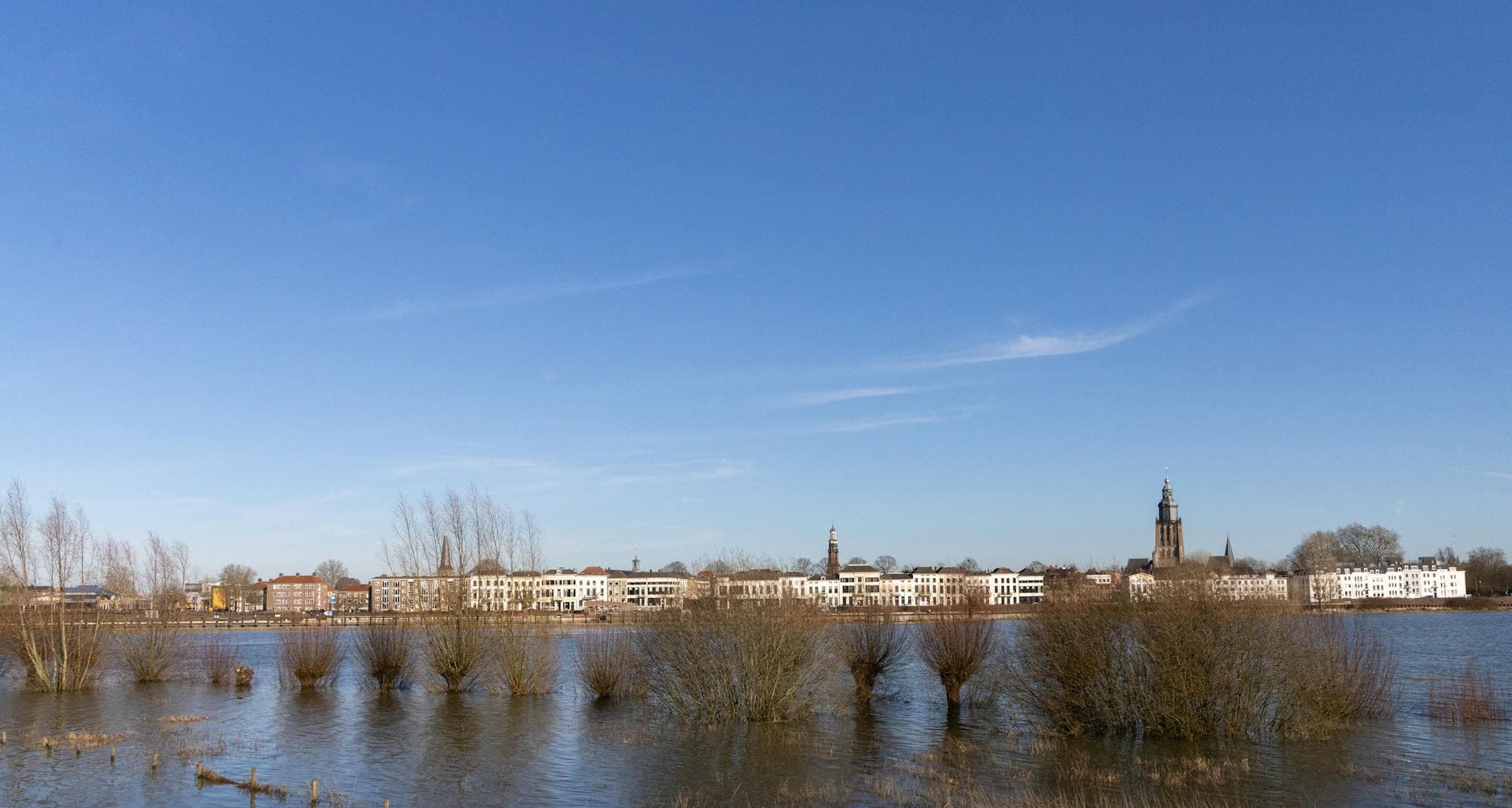 A serene view of Zutphen's skyline with historic buildings and a church by a calm river.