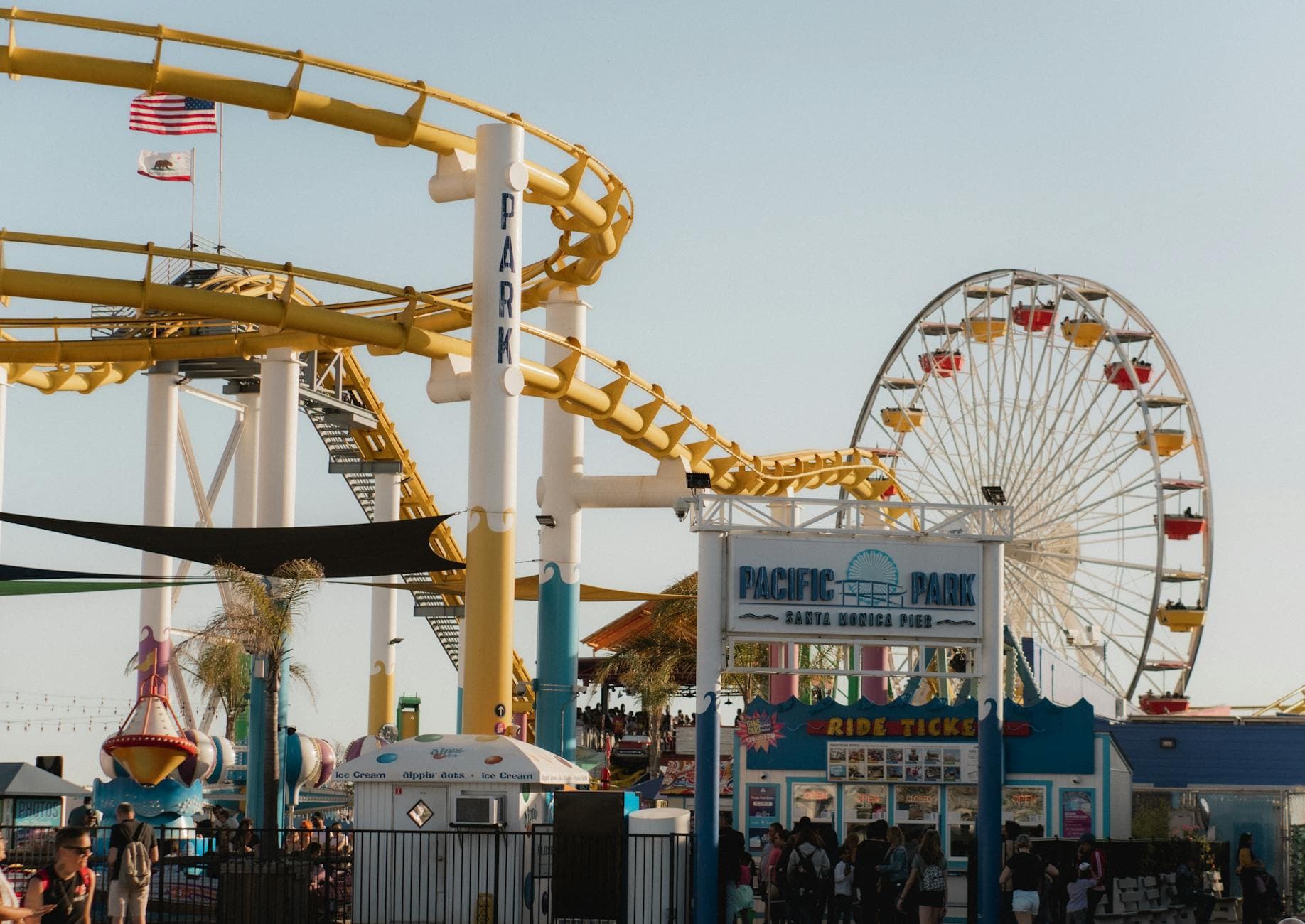 Vibrant amusement park scene at Santa Monica Pier with roller coaster and Ferris wheel in view.