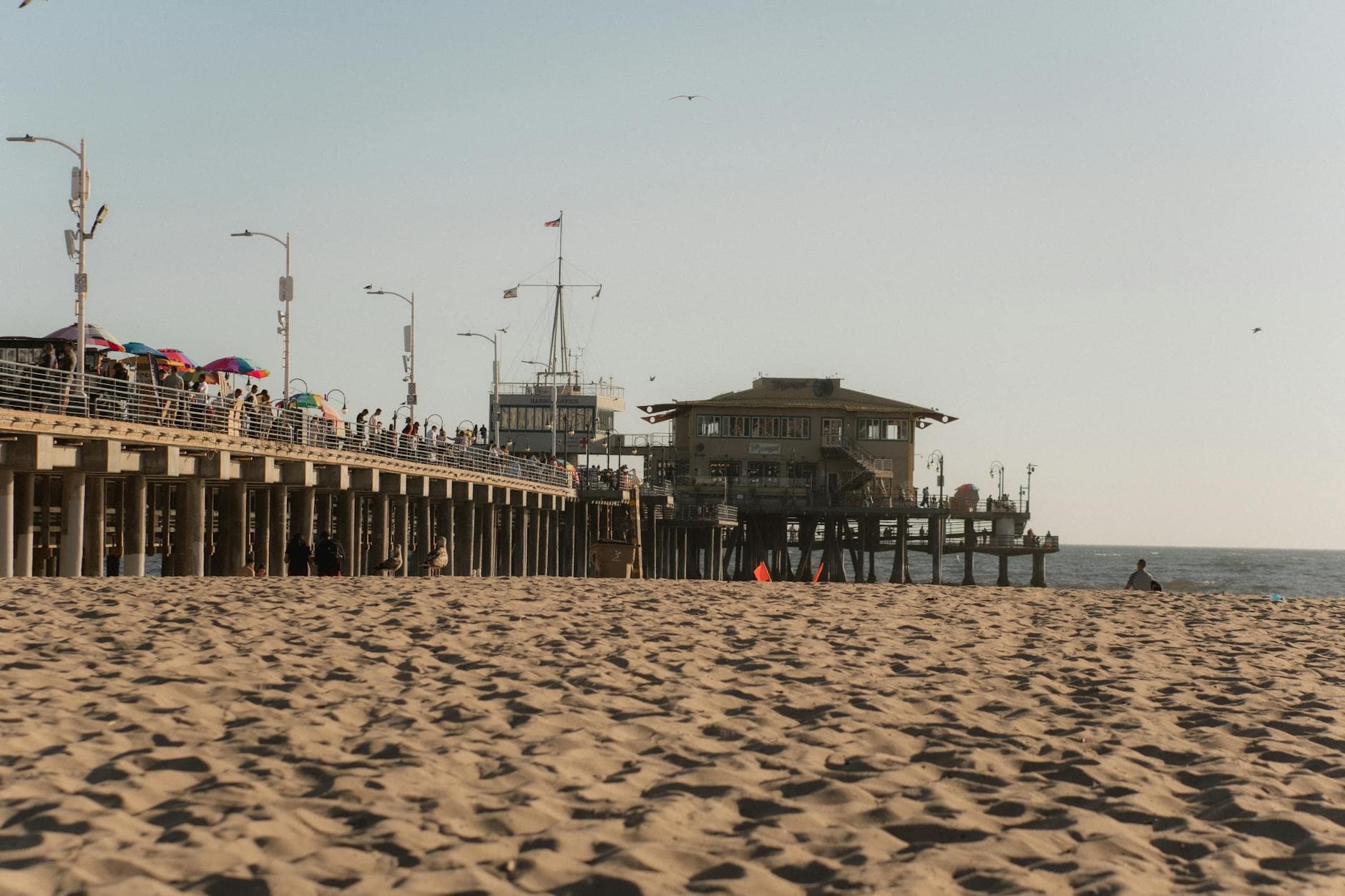 A scenic view of Santa Monica Pier with people enjoying the beach at sunset.