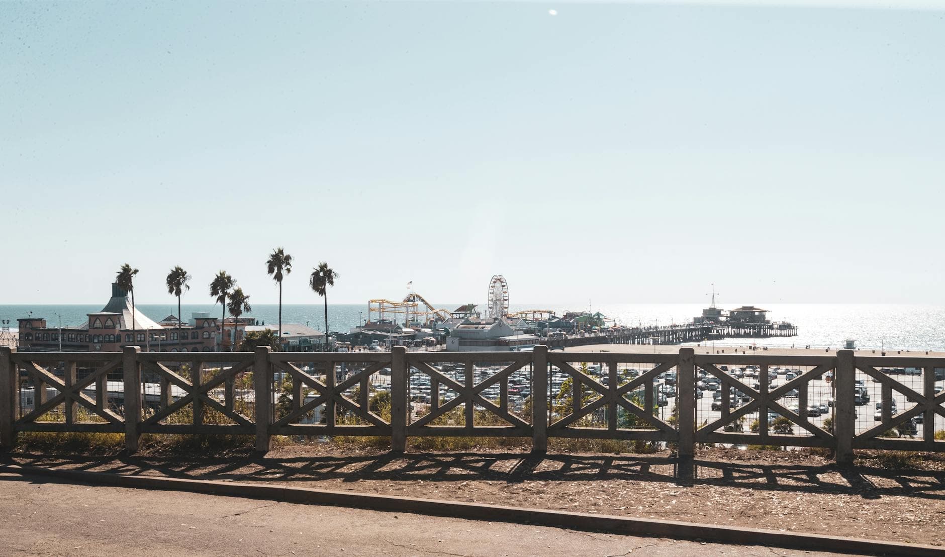 A scenic view of Santa Monica Pier with palm trees and Ferris wheel under bright sunlight.