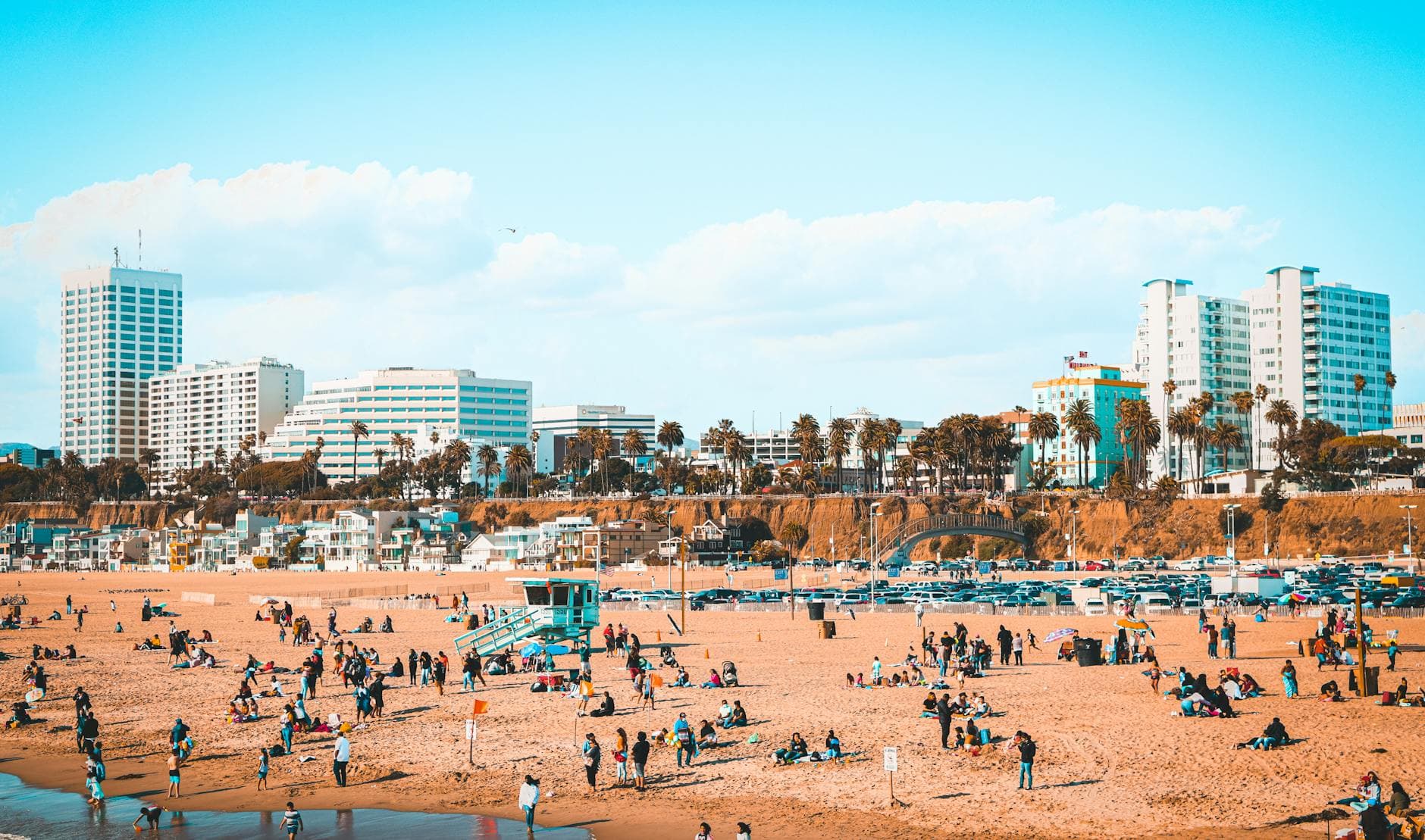 Vibrant beach scene in Santa Monica, CA with busy shore and city skyline.