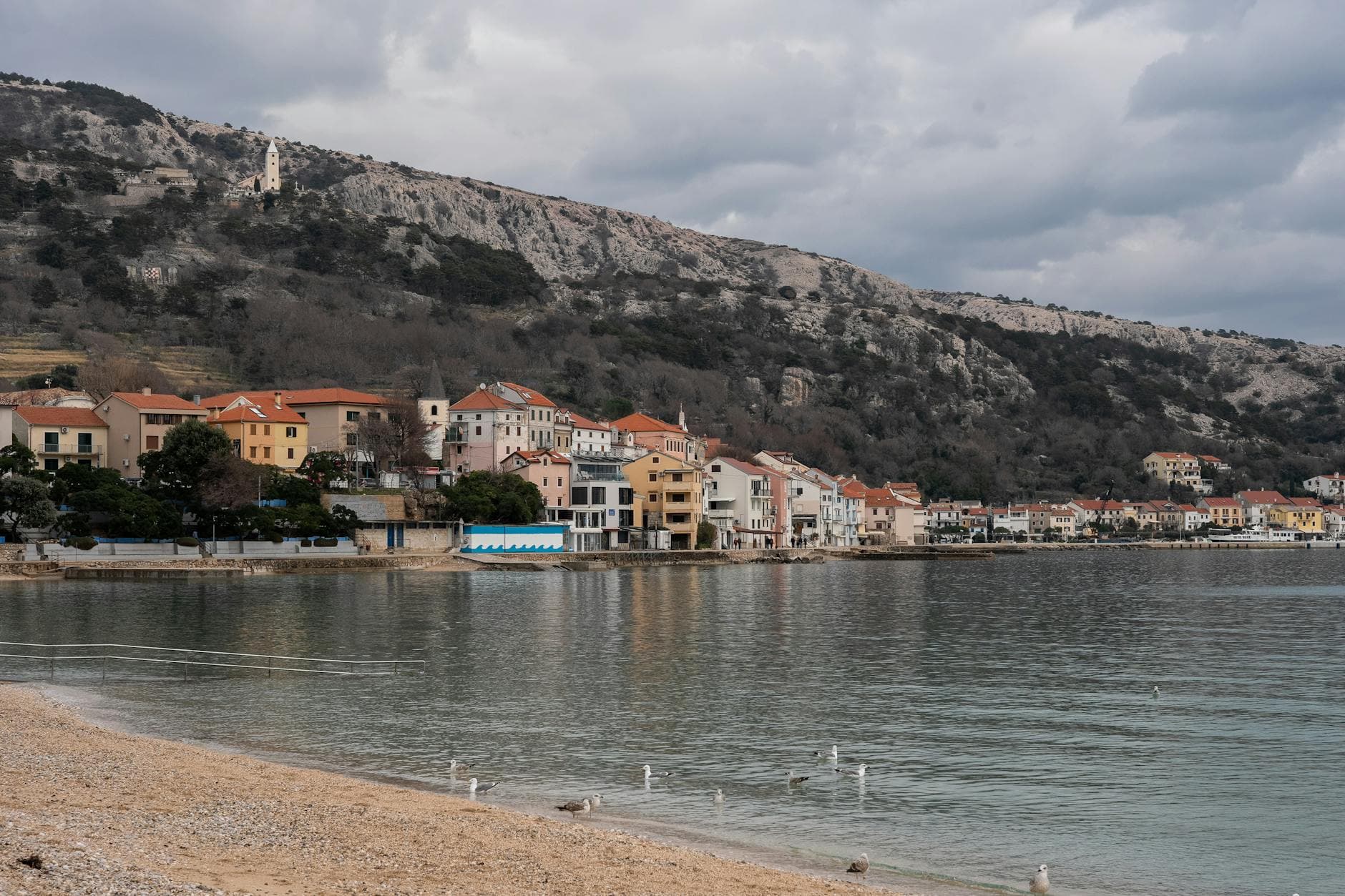 Scenic seaside view of Krk, Croatia with coastal buildings and an overcast sky.
