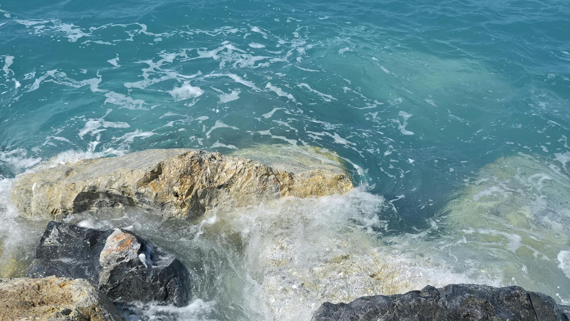 Dynamic view of waves crashing on rocky shoreline, capturing the vibrant sea in Calabria, Italy.
