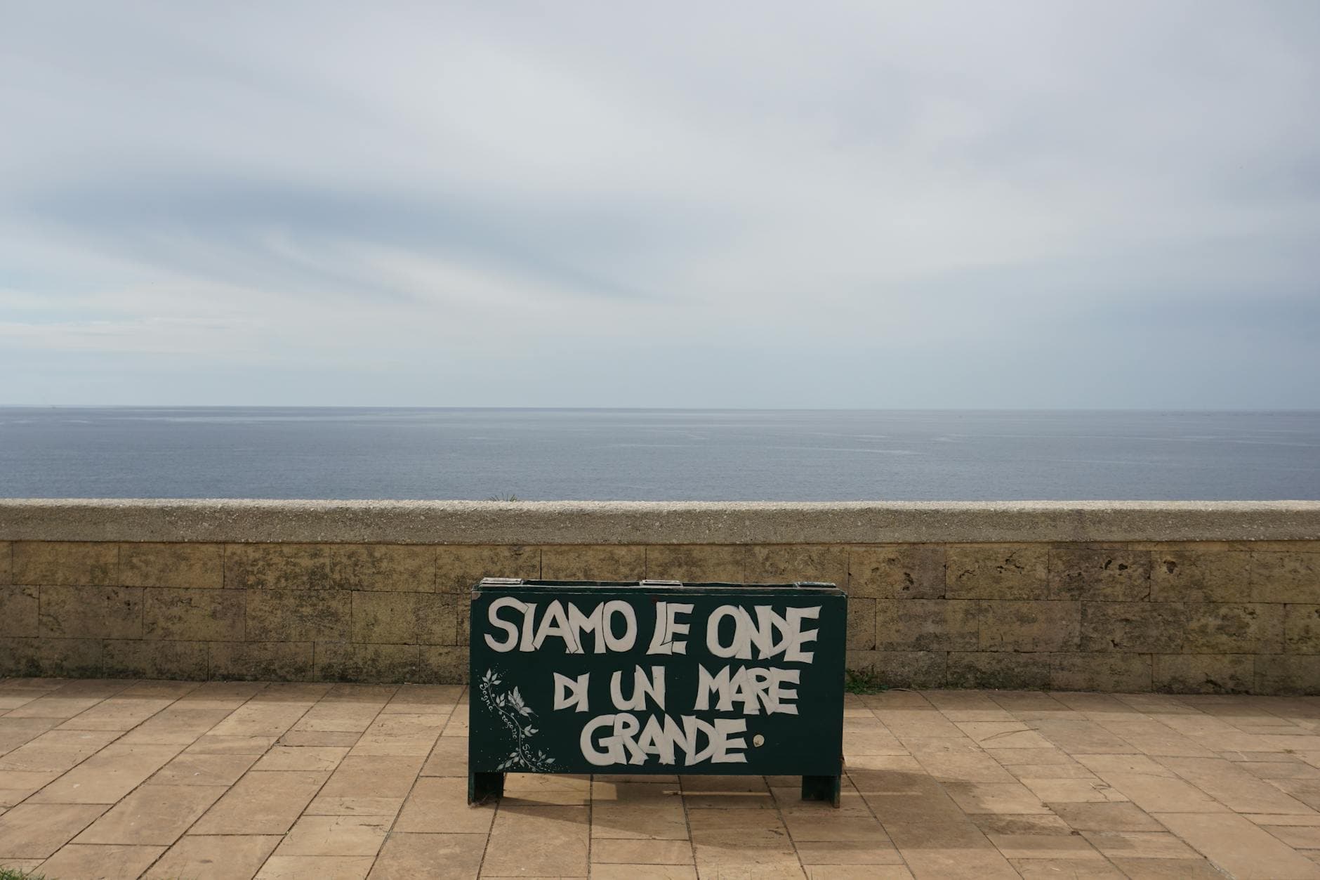 Graffiti on a seaside promenade overlooking a vast, calm ocean under an overcast sky.