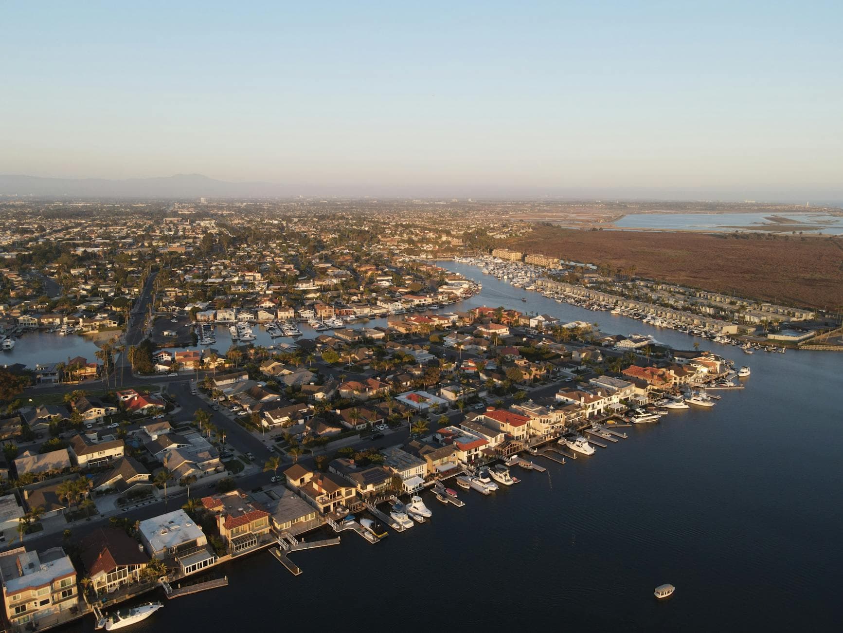 Stunning aerial view of Huntington Beach harbor showcasing boats and residential area at sunset.