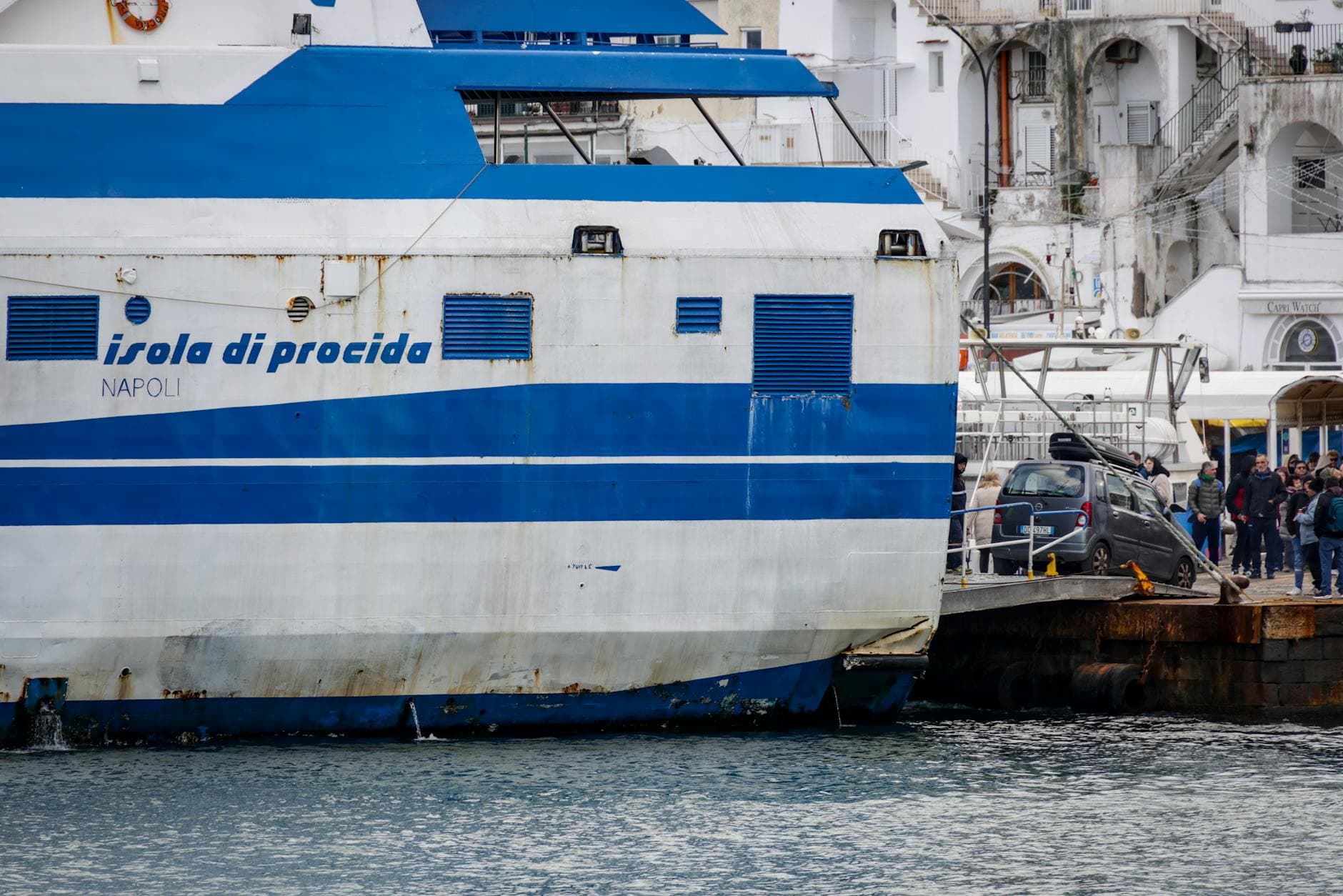View of ferry 'Isola di Procida' docked with people and seaside architecture.