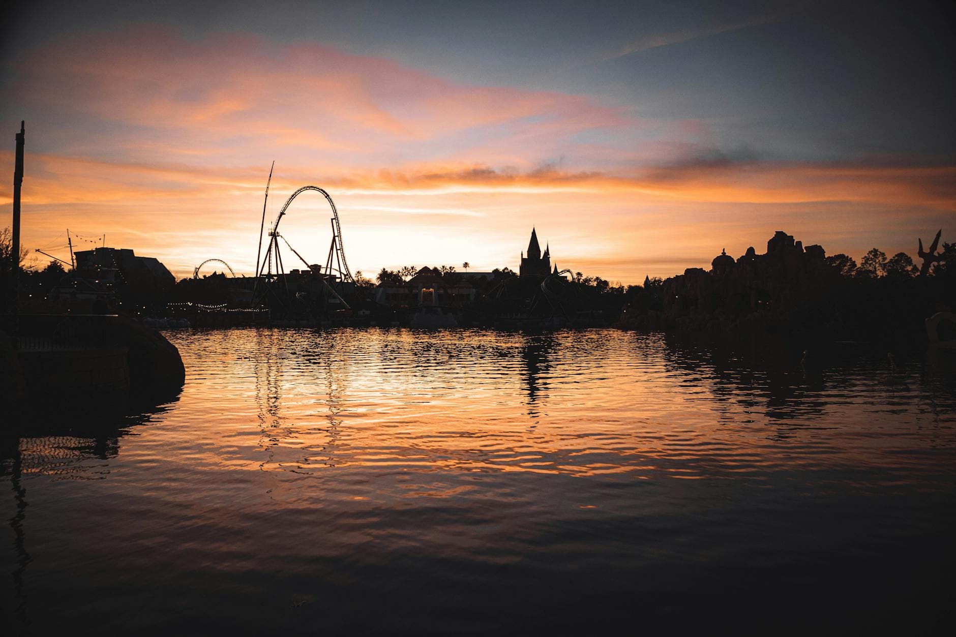 Dramatic sunset reflection on a lake with silhouetted roller coaster and skyline in Orlando.