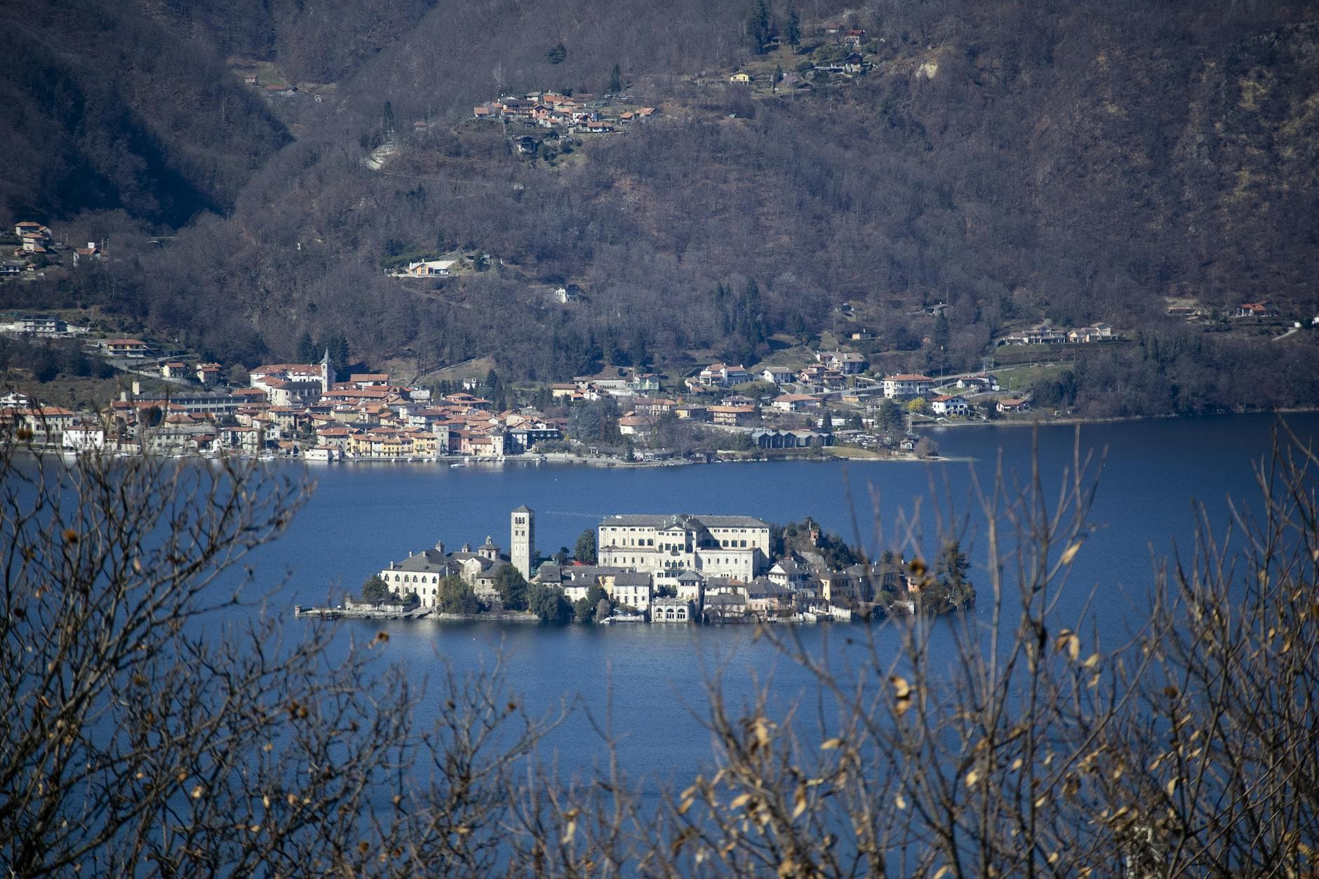 A picturesque view of Isola San Giulio surrounded by Lake Orta in Italy, framed by distant mountains.