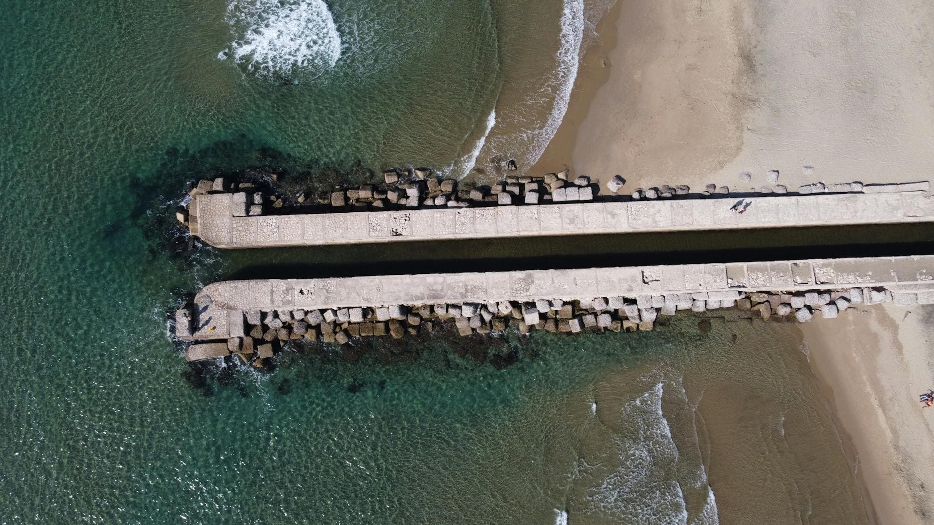 Aerial perspective of a concrete pier extending into the sea at Anzio's coastline in Italy.