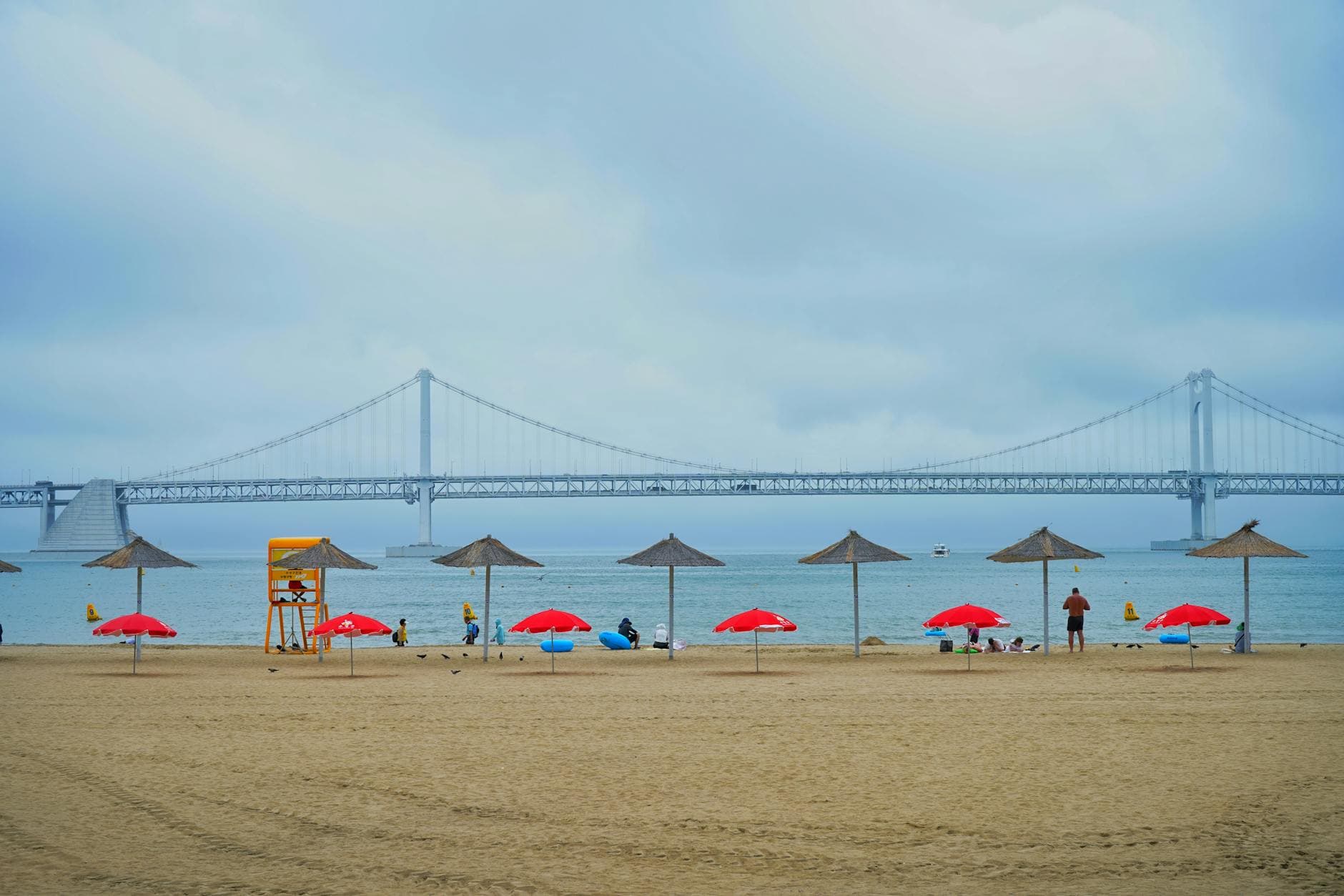 Relaxing beach scene featuring Gwangan Bridge in Korea with umbrellas and a lifeguard stand.