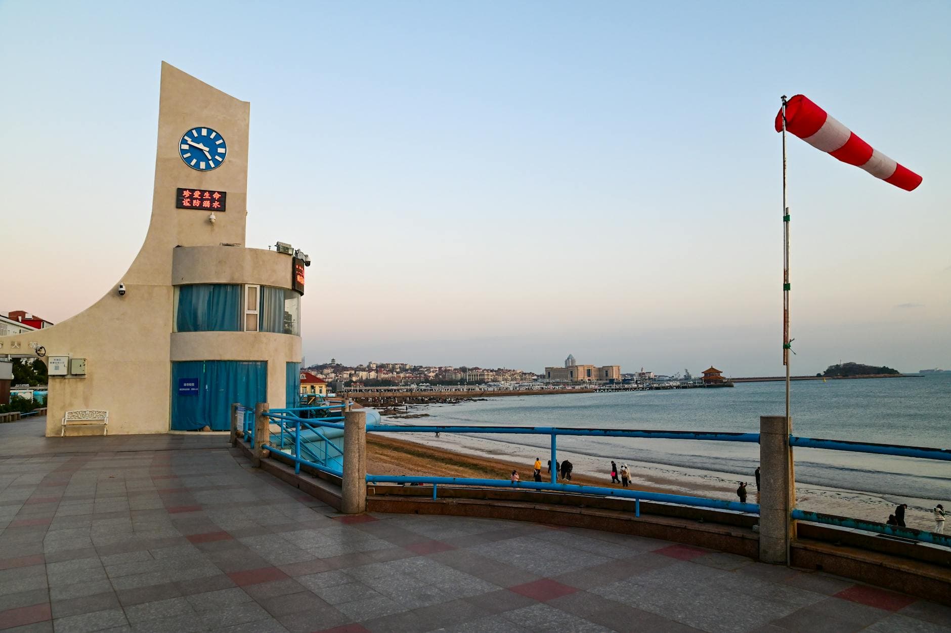 A scenic view of Qingdao's coastal promenade featuring a curved clock tower and ocean horizon at sunset.