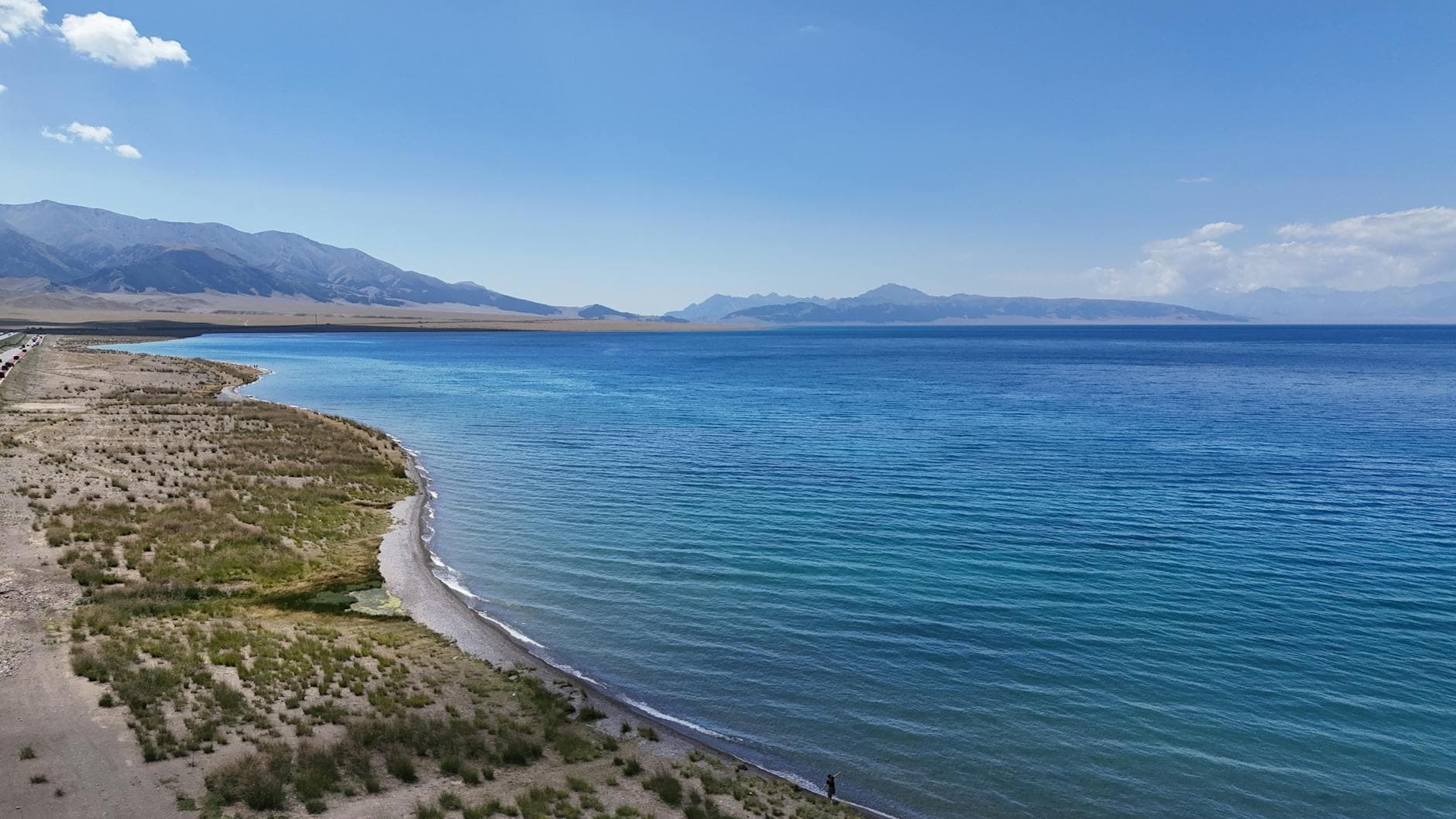 Scenic aerial view of Sayram Lake's pristine shoreline and clear blue waters under a bright summer sky.