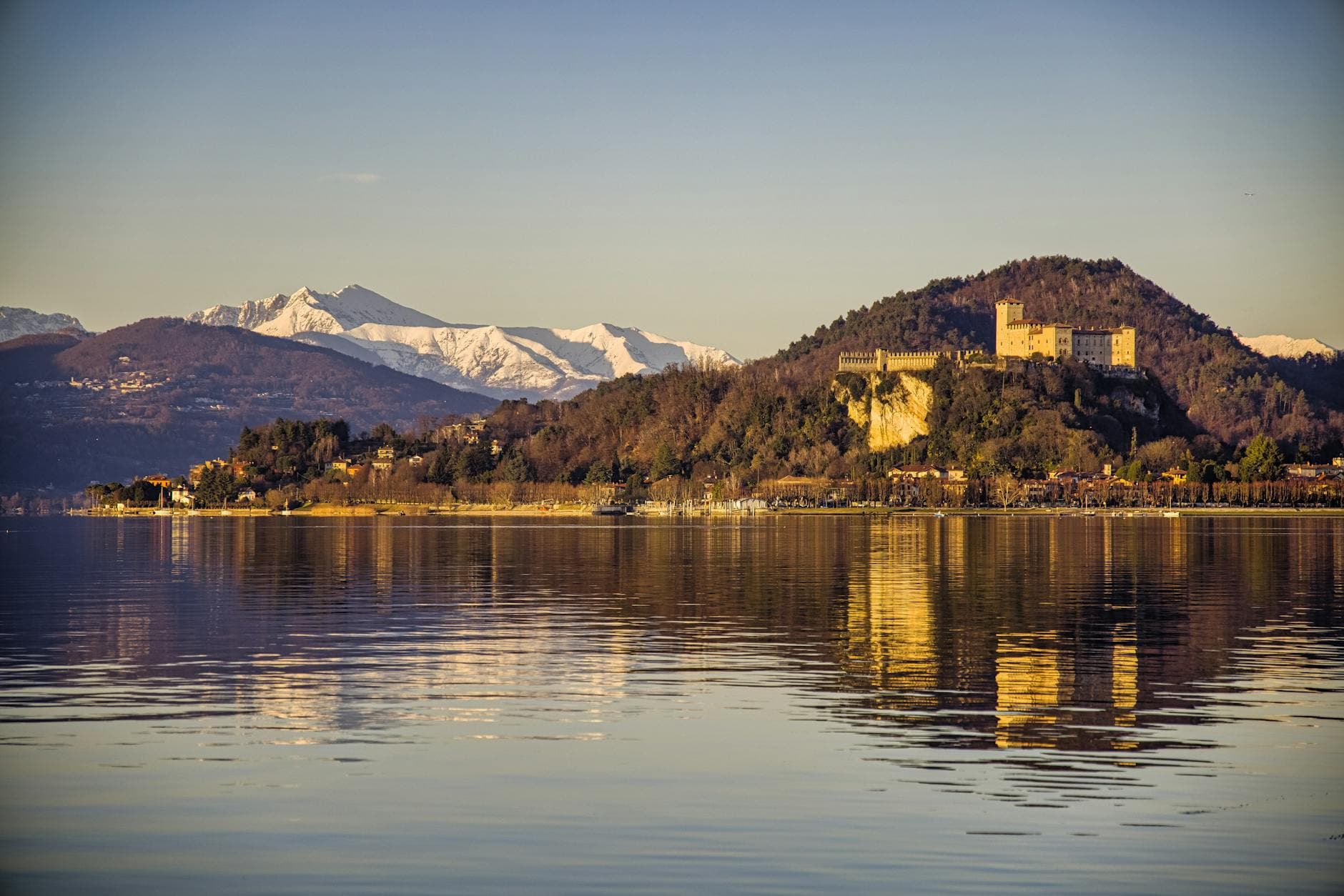 Stunning view of an ancient castle by the lake with mountain backdrop, captured at sunset.