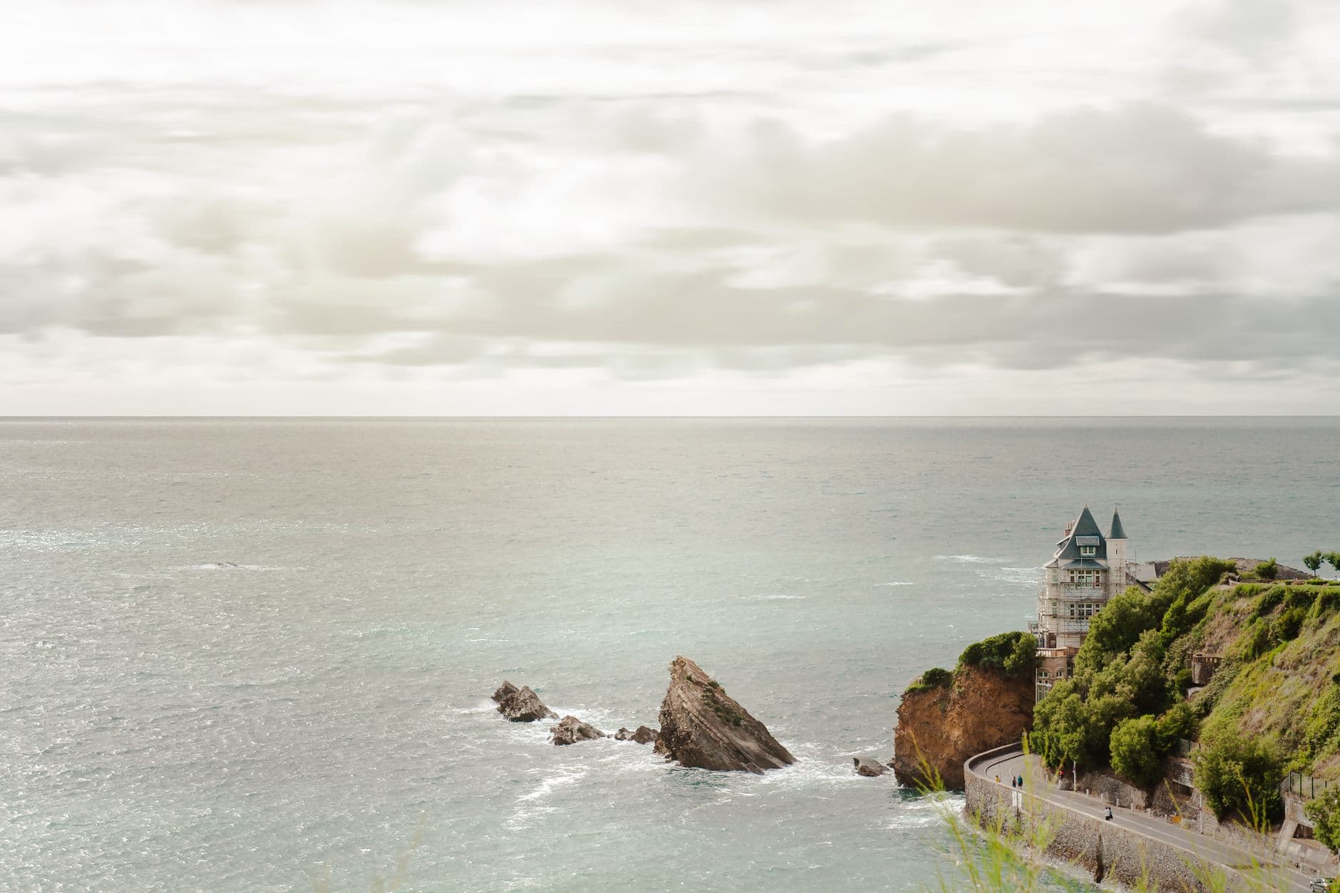 Beautiful coastal view of Biarritz, France, featuring rocky cliffs and serene ocean waves under a cloudy sky.