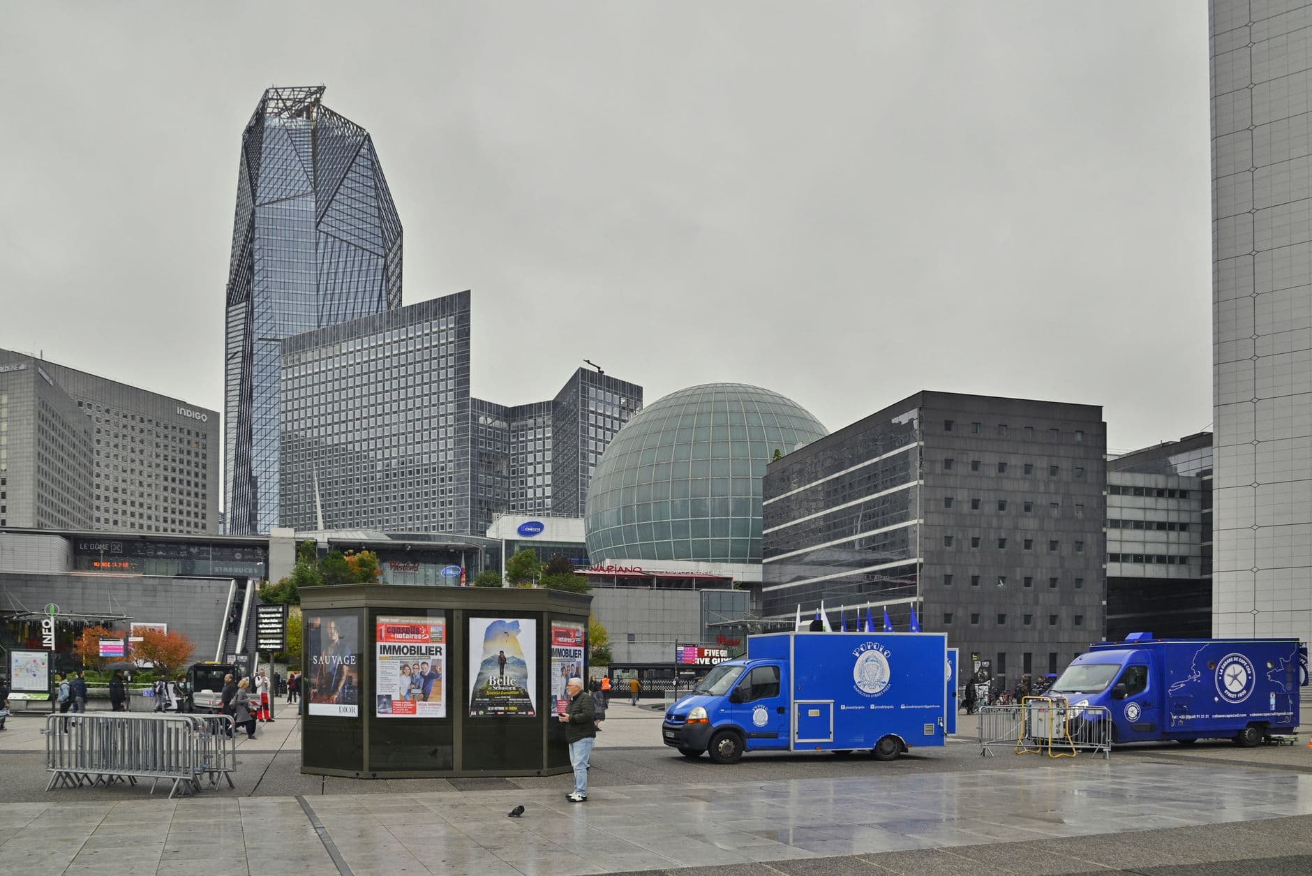 A cityscape view of the La Défense district with modern buildings and people walking.