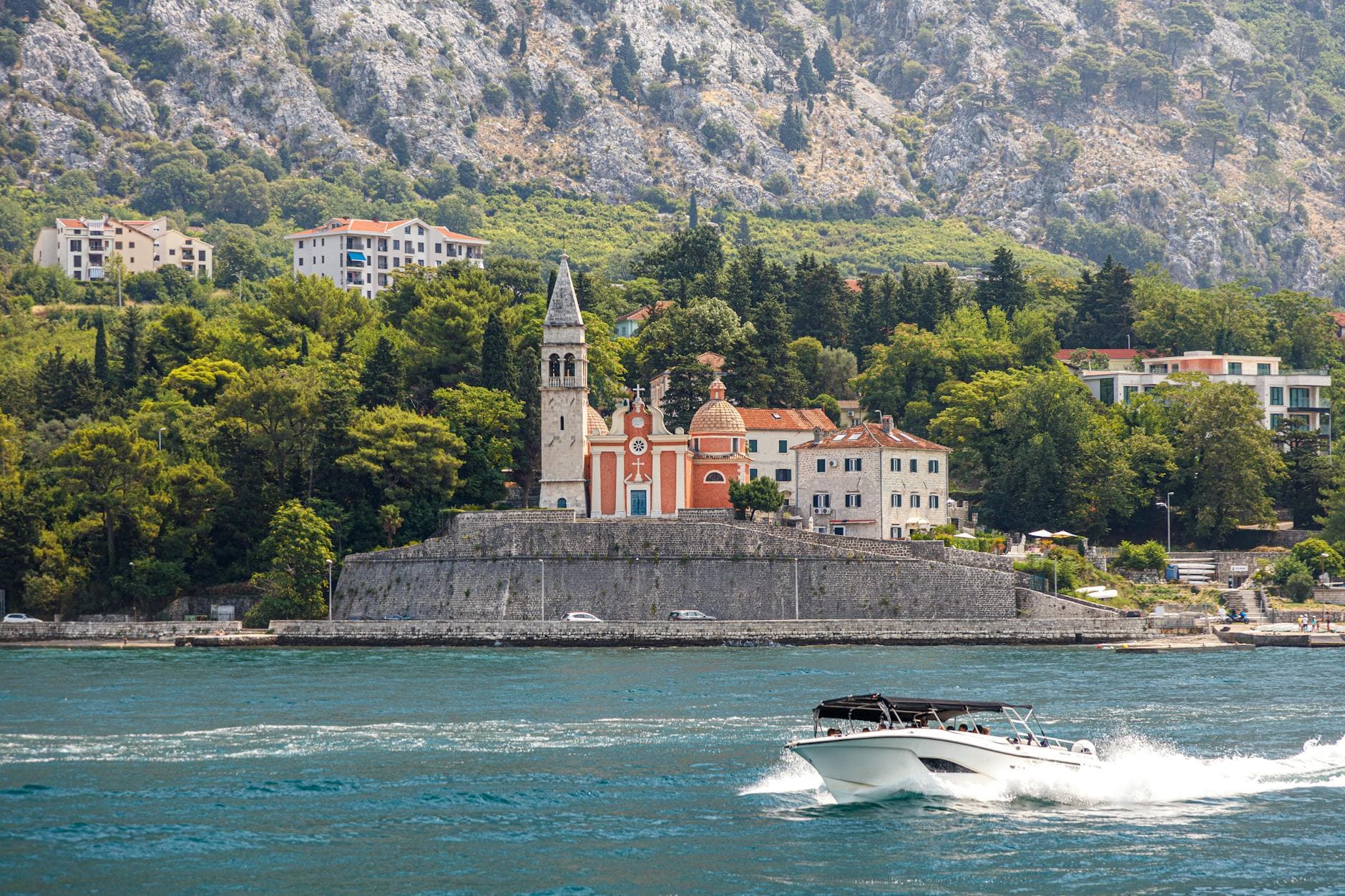 Picturesque view of historic Perast with a church and a speedboat on the Adriatic Sea.
