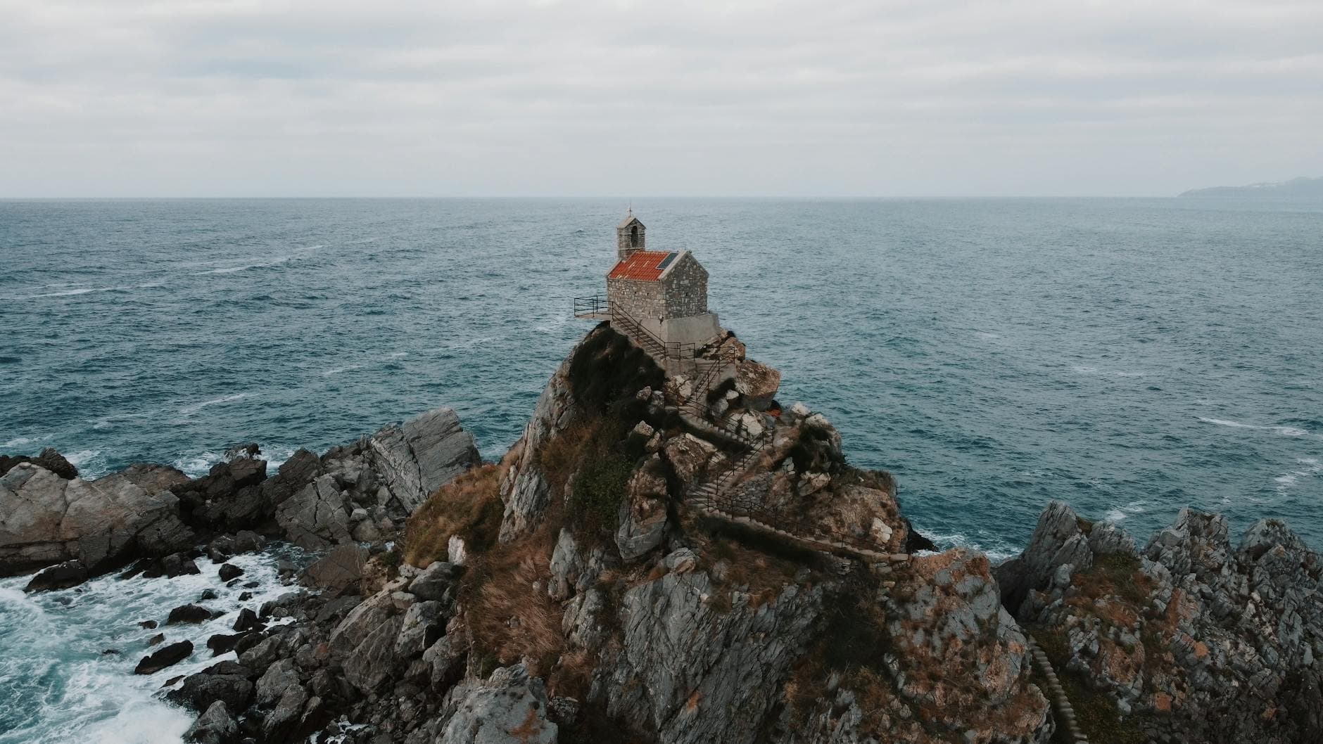 Aerial view of a historic church on a rocky outcrop by the Adriatic Sea in Petrovac, Montenegro.