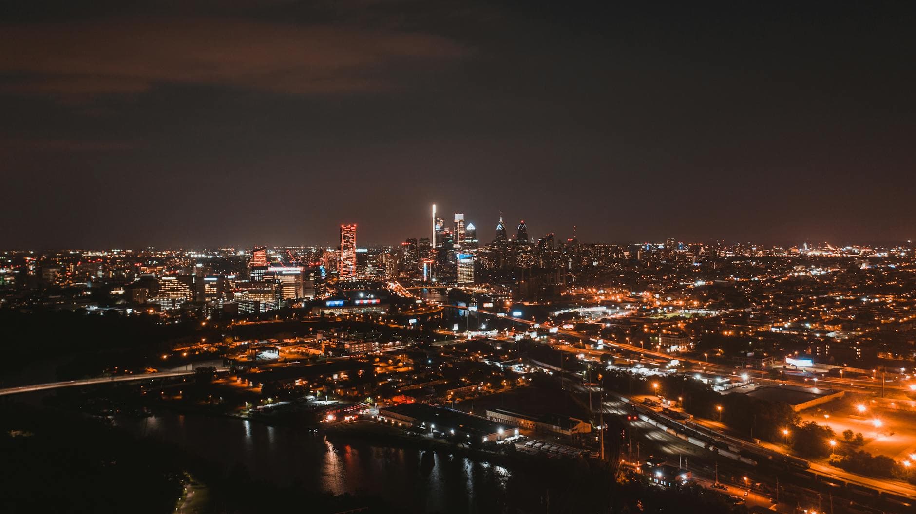Drone view of brightly glowing city streets located on river bank at night time