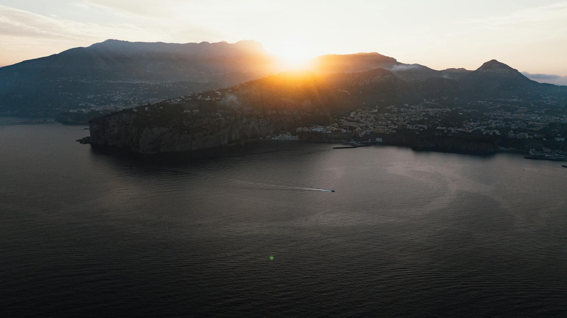 Captivating birds-eye view of Piano di Sorrento, Italy, as the sun sets behind hills and reflects on the sea.