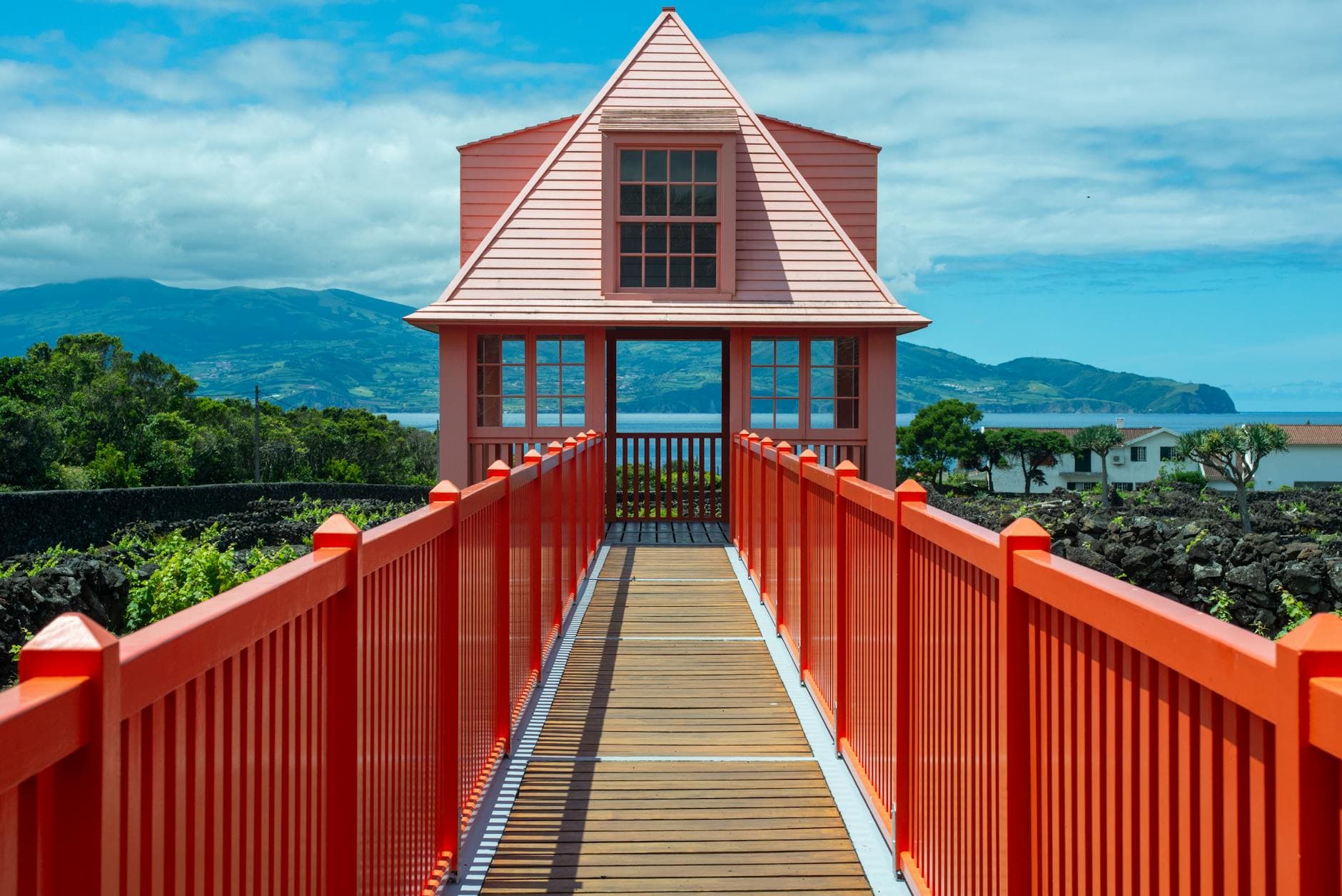 A vibrant red bridge leads to a picturesque house set in the scenic Azores landscape.