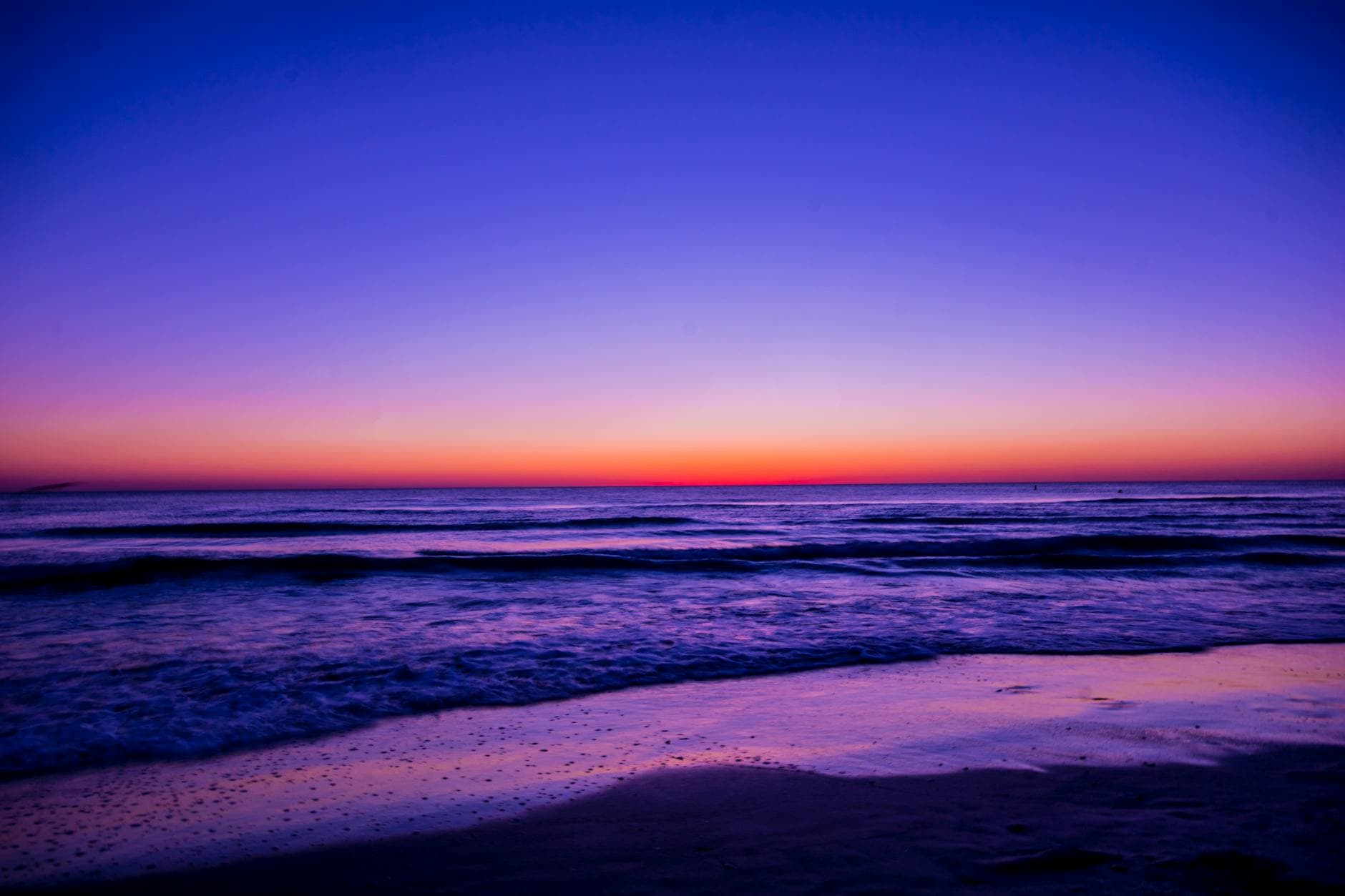 Serene beach sunset with vibrant colors reflecting on the water and waves.