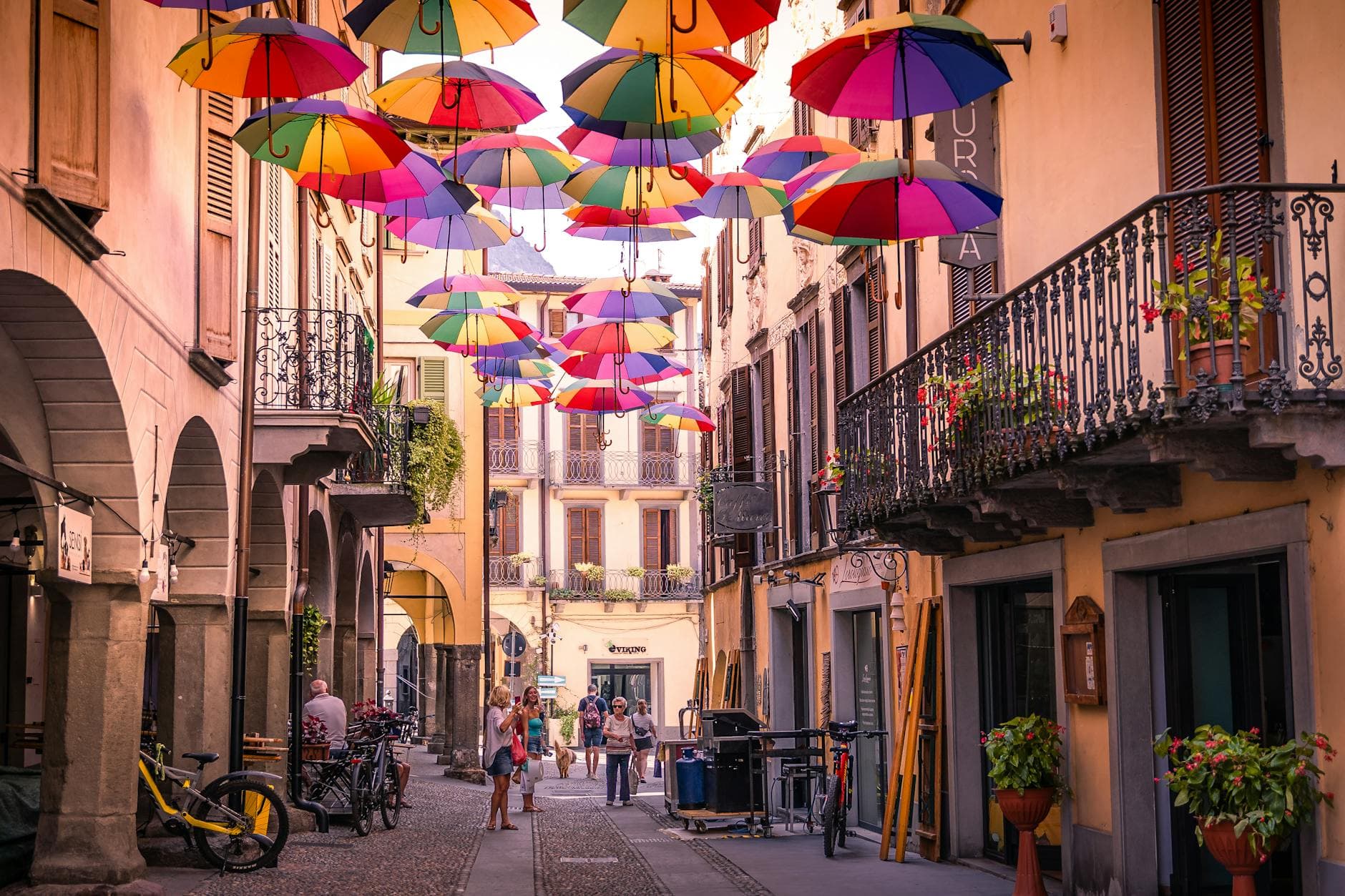 Vibrant umbrellas decorate a picturesque street in Pisogne, Italy, capturing a lively European charm.