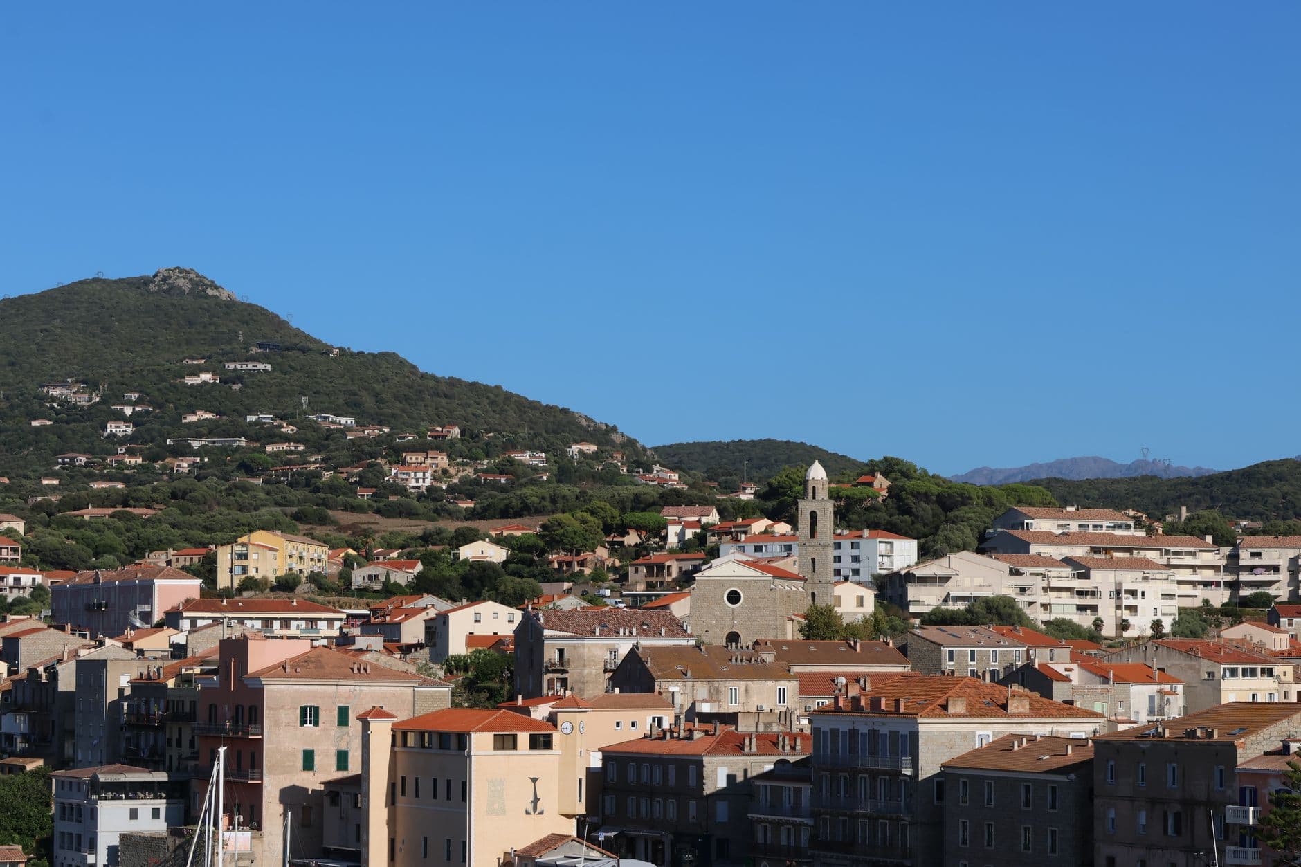 Scenic view of a coastal town with a mountainous backdrop under clear blue skies.