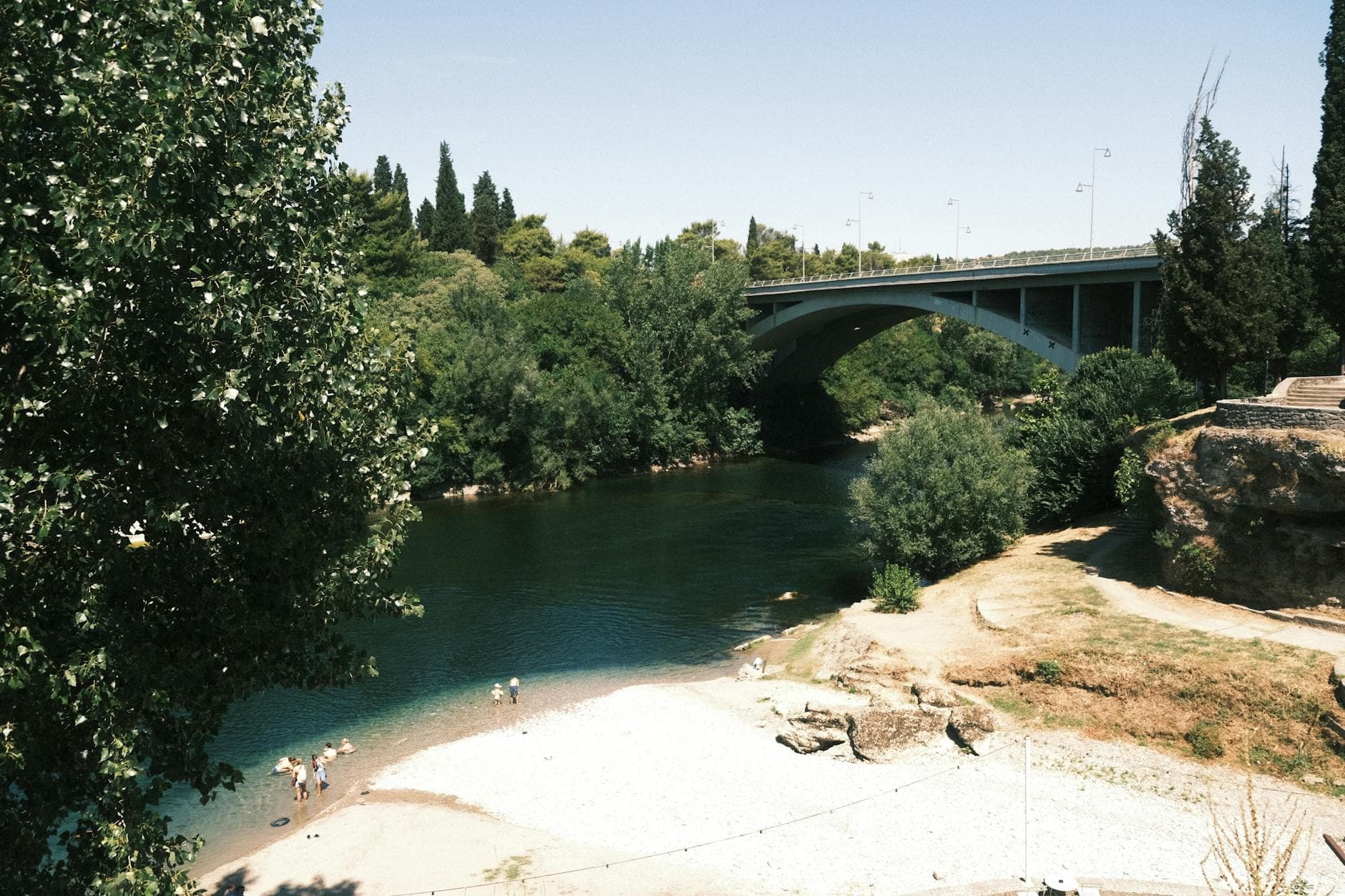 A serene riverside scene featuring a bridge and lush greenery in Podgorica, Montenegro.