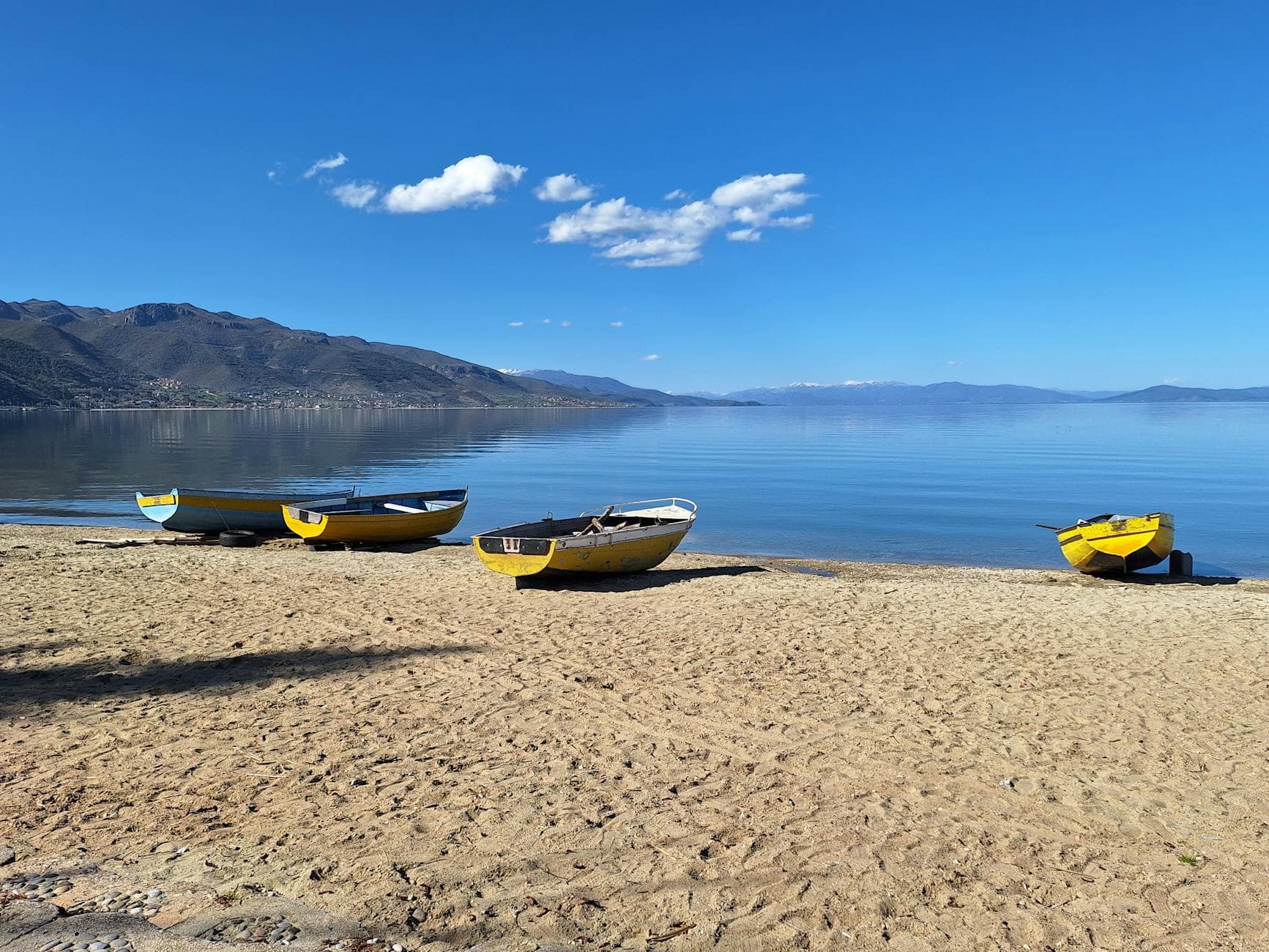 Tranquil view of Calm Lake Ohrid with colorful boats on sand in Pogradec, perfect for summer relaxation.