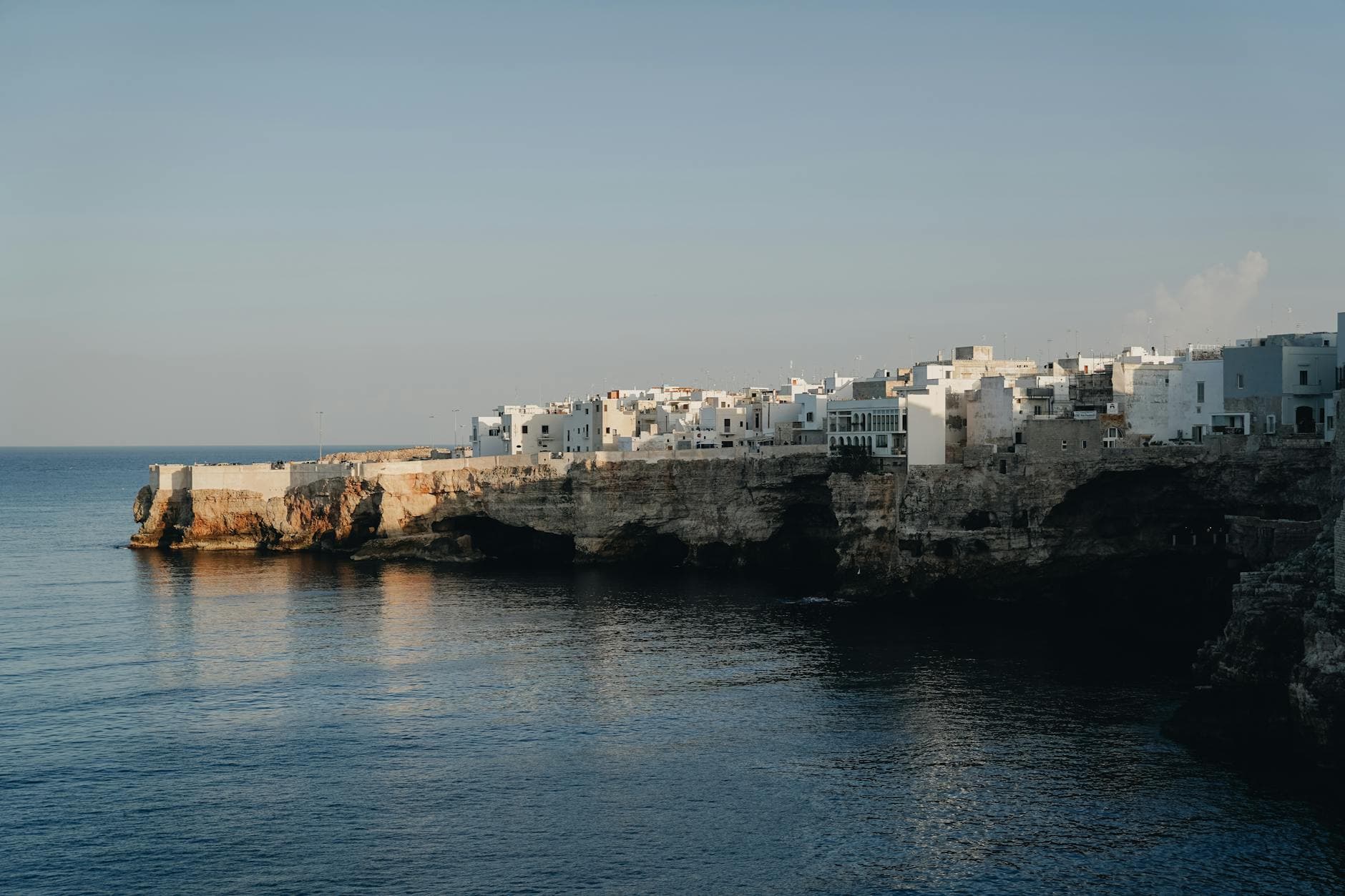 A stunning coastal view of Polignano a Mare in Italy, featuring white cliffside buildings reflecting in the calm sea.