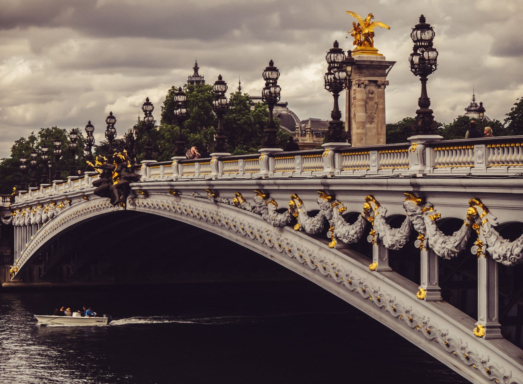 Elegant view of Pont Alexandre III over the Seine in Paris with decorative lampposts and overcast sky.
