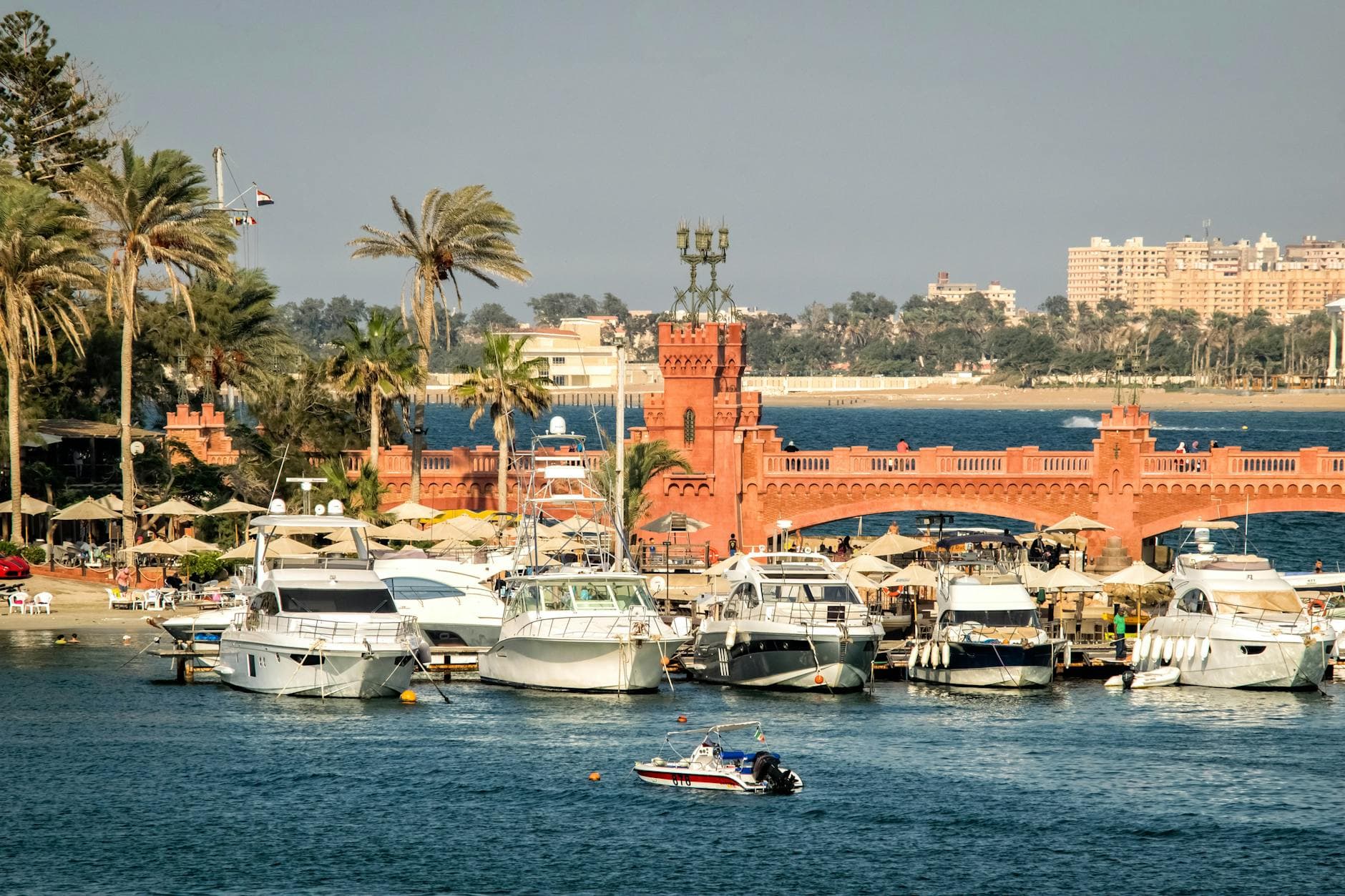 A scenic view of yachts docked by a historic bridge in Alexandria, Egypt.