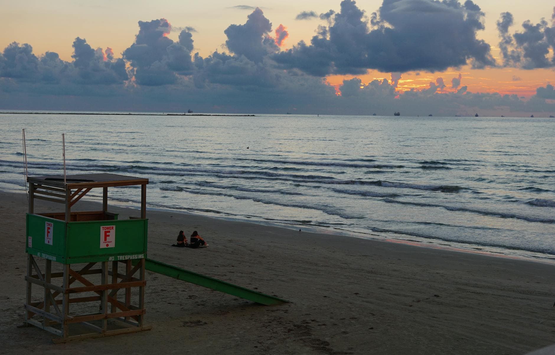 Couple sitting on Port Aransas beach at sunset with lifeguard tower and scenic ocean view.