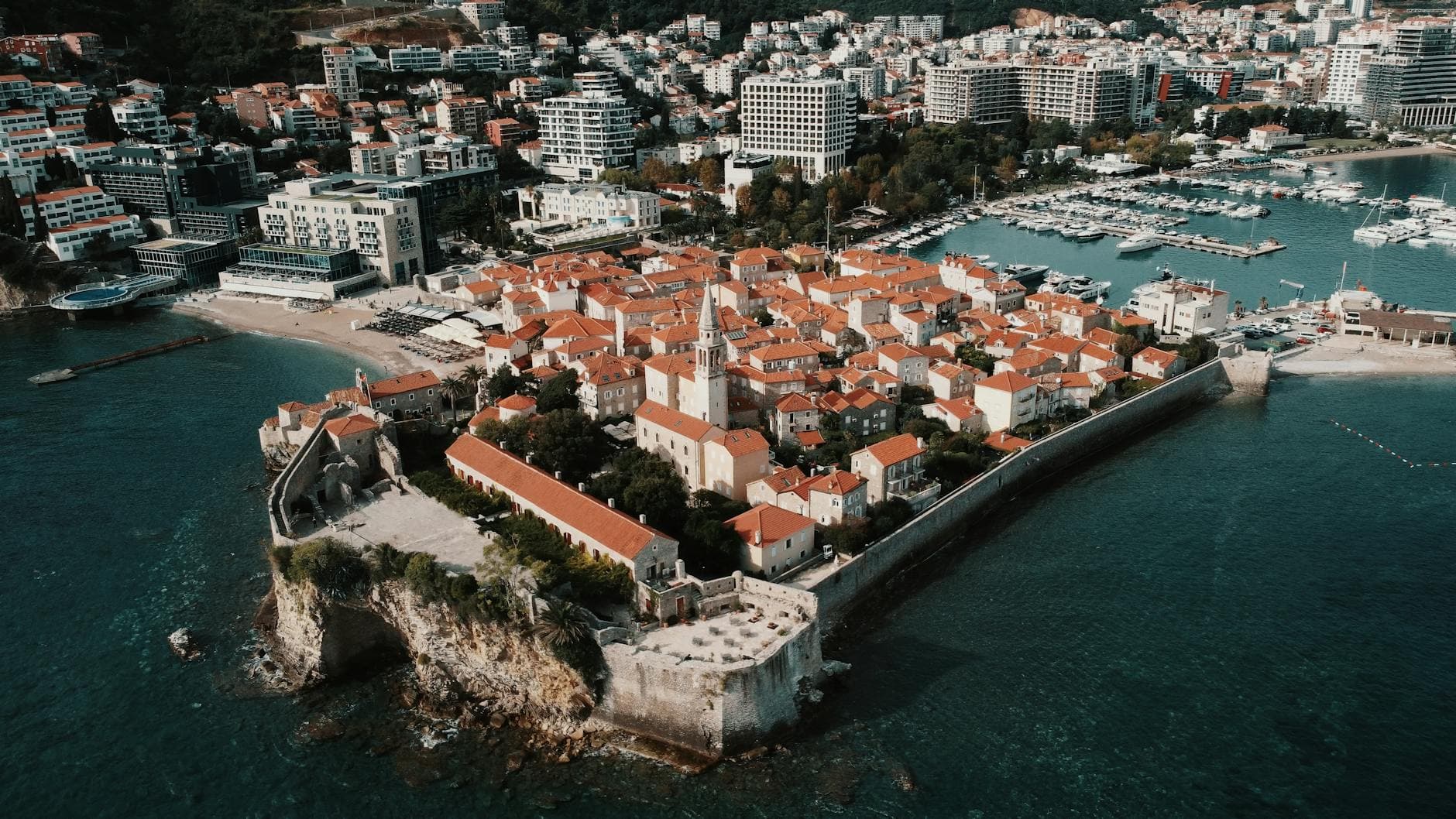 Drone view of Budva's scenic old town with red roofs and coastal beauty.