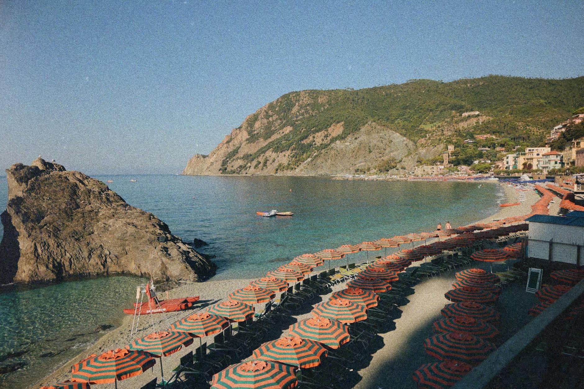Explore the stunning coast of Monterosso al Mare, Liguria with vibrant beach umbrellas and rocky shores.